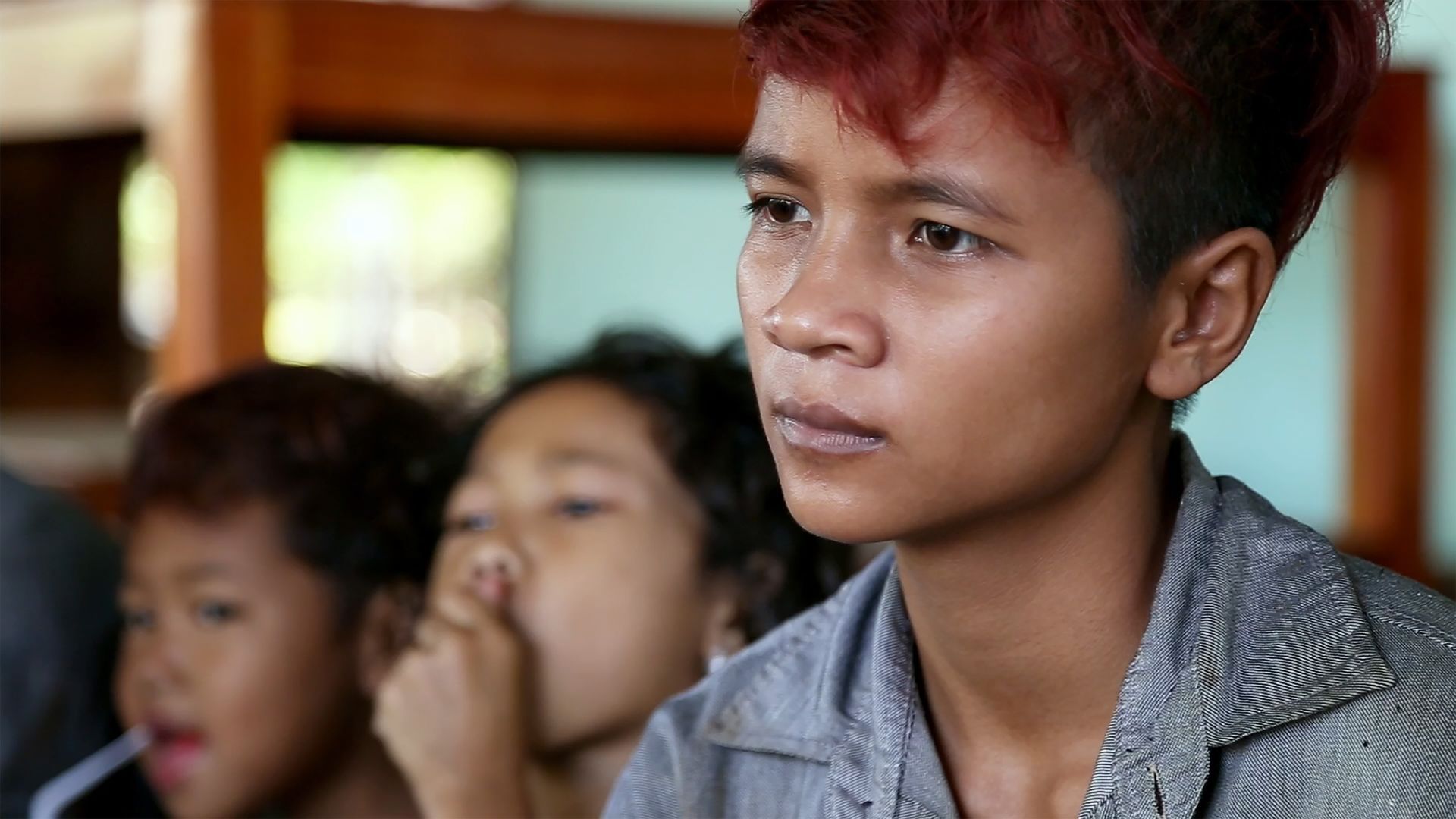 Eine junge Person mit roten Haaren sitzt mit anderen Kindern in einem Klassenzimmer
