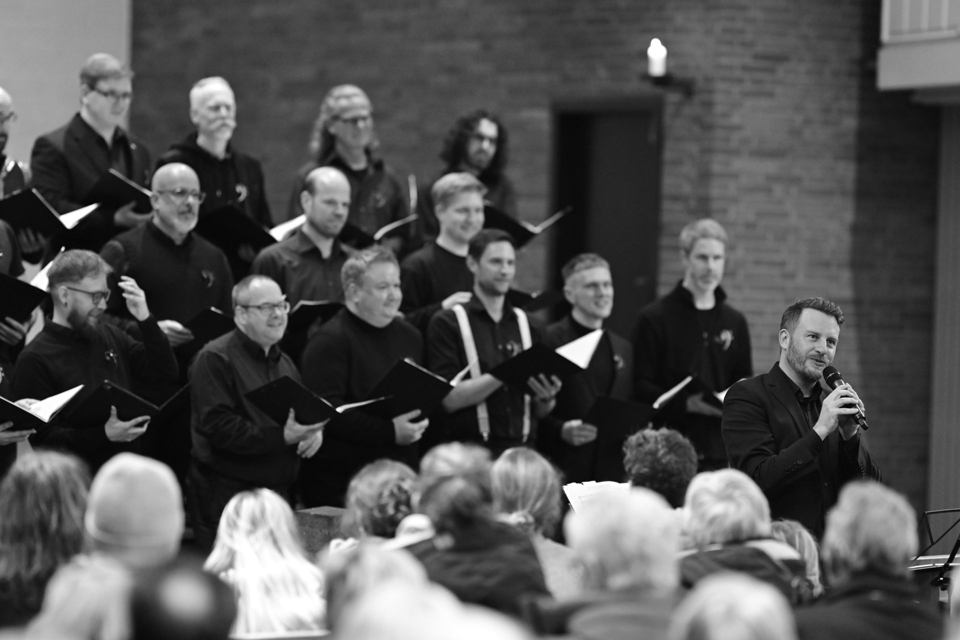 Chorgesang, Dirigent spricht zum Publikum, Schwarzweiß, Innenansicht einer Kirche.
