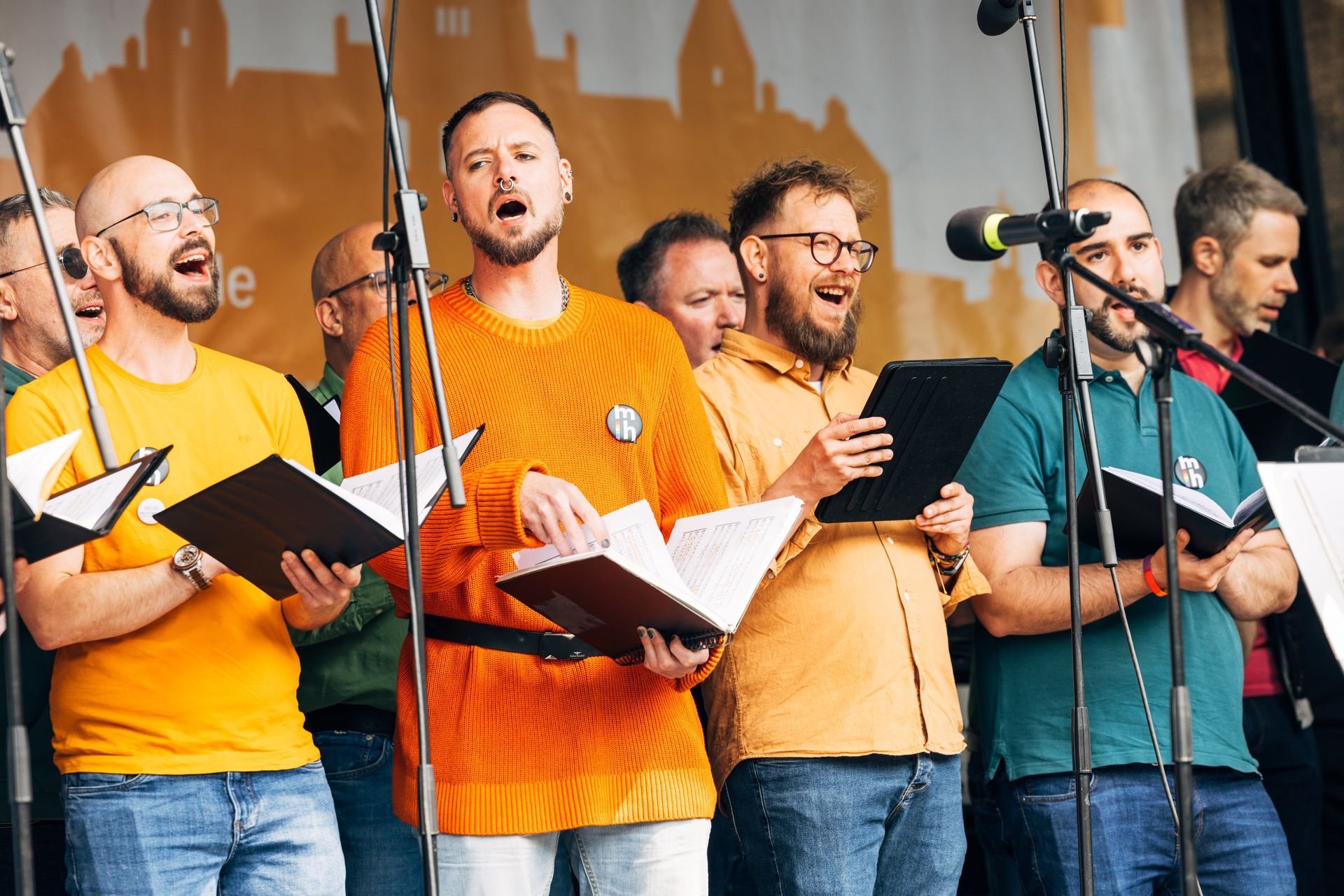 Ein Männerchor singt im Freien, hält Notenblätter in den Händen und trägt bunte Hemden.