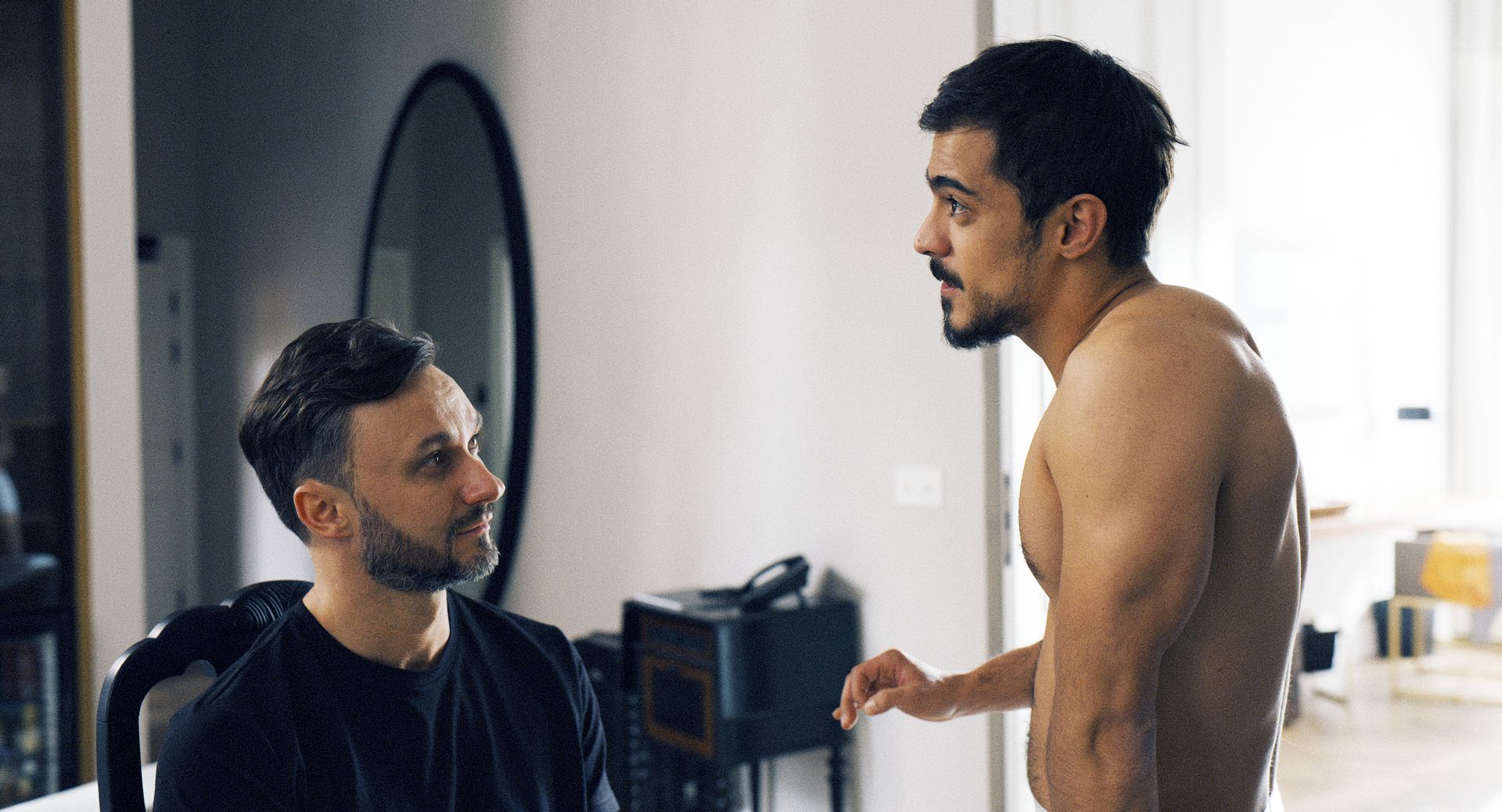 Ein Mann mit schwarzem Shirt spricht mit einem anderen Mann ohne Hemd