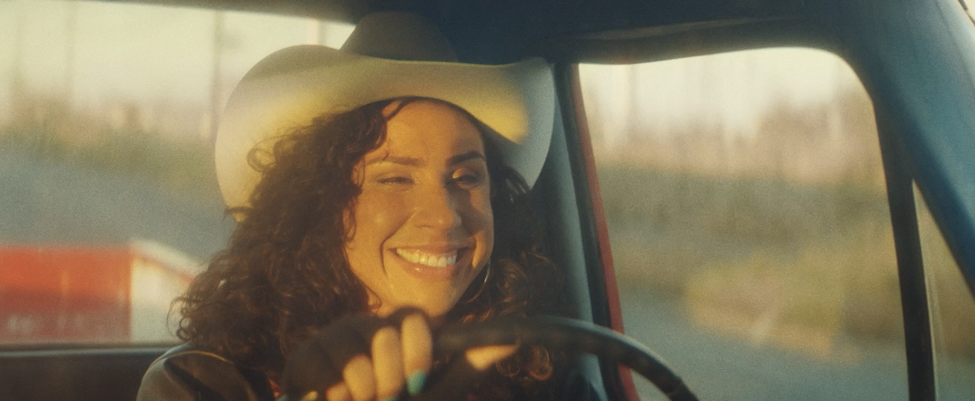 Person mit Cowboyhut lächelt und zwinkert beim Autofahren.