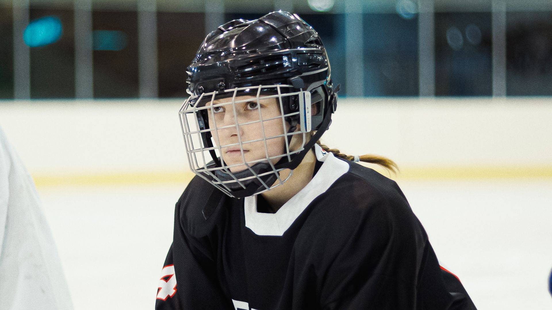Hockeyspielerin in schwarzem Trikot und Helm auf dem Eis, konzentrierter Blick.