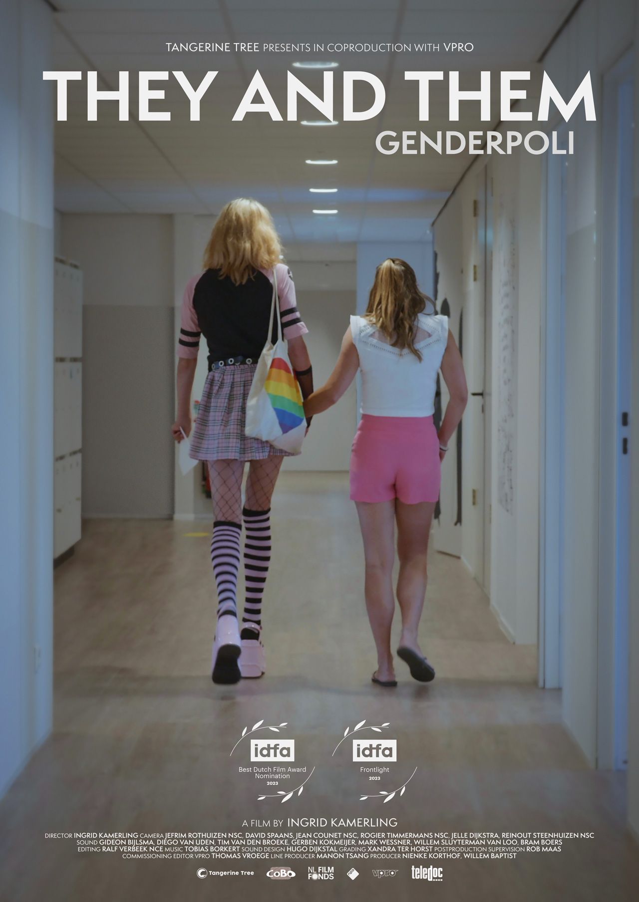 Eine Person mit Brille und rosa geblümtem Hemd lehnt an einer weißen Wand und wird in einem Spiegel reflektiert.