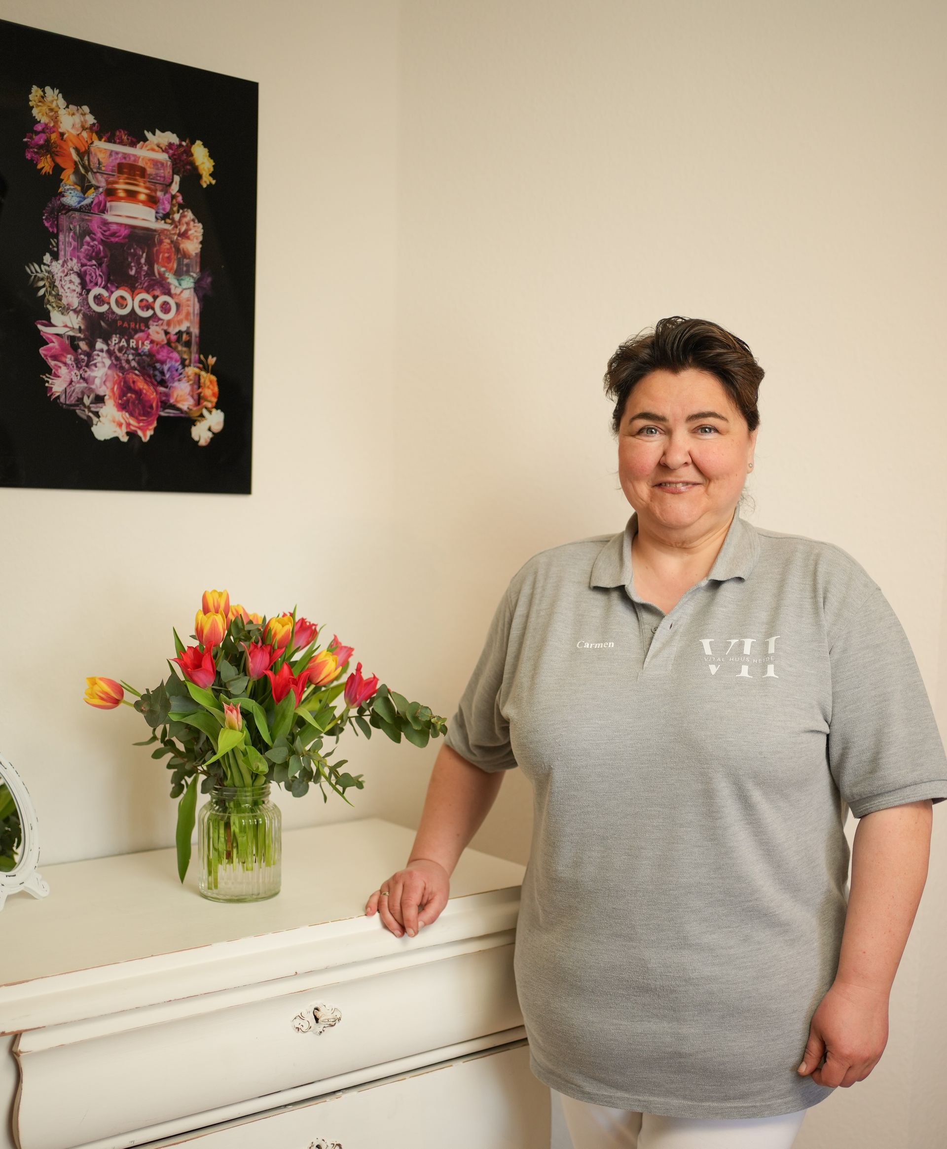 Eine Frau steht vor einer Wand und trägt ein weißes Oberteil und eine Halskette.