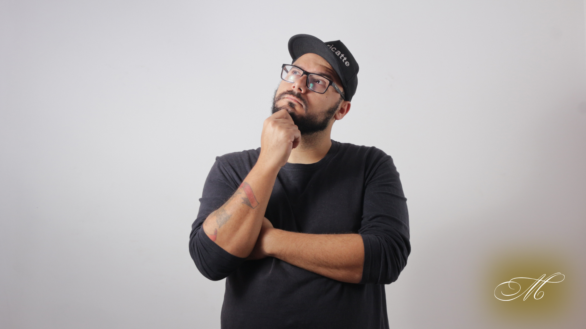 A man with a beard and glasses is standing with his arms crossed and his hand on his chin.