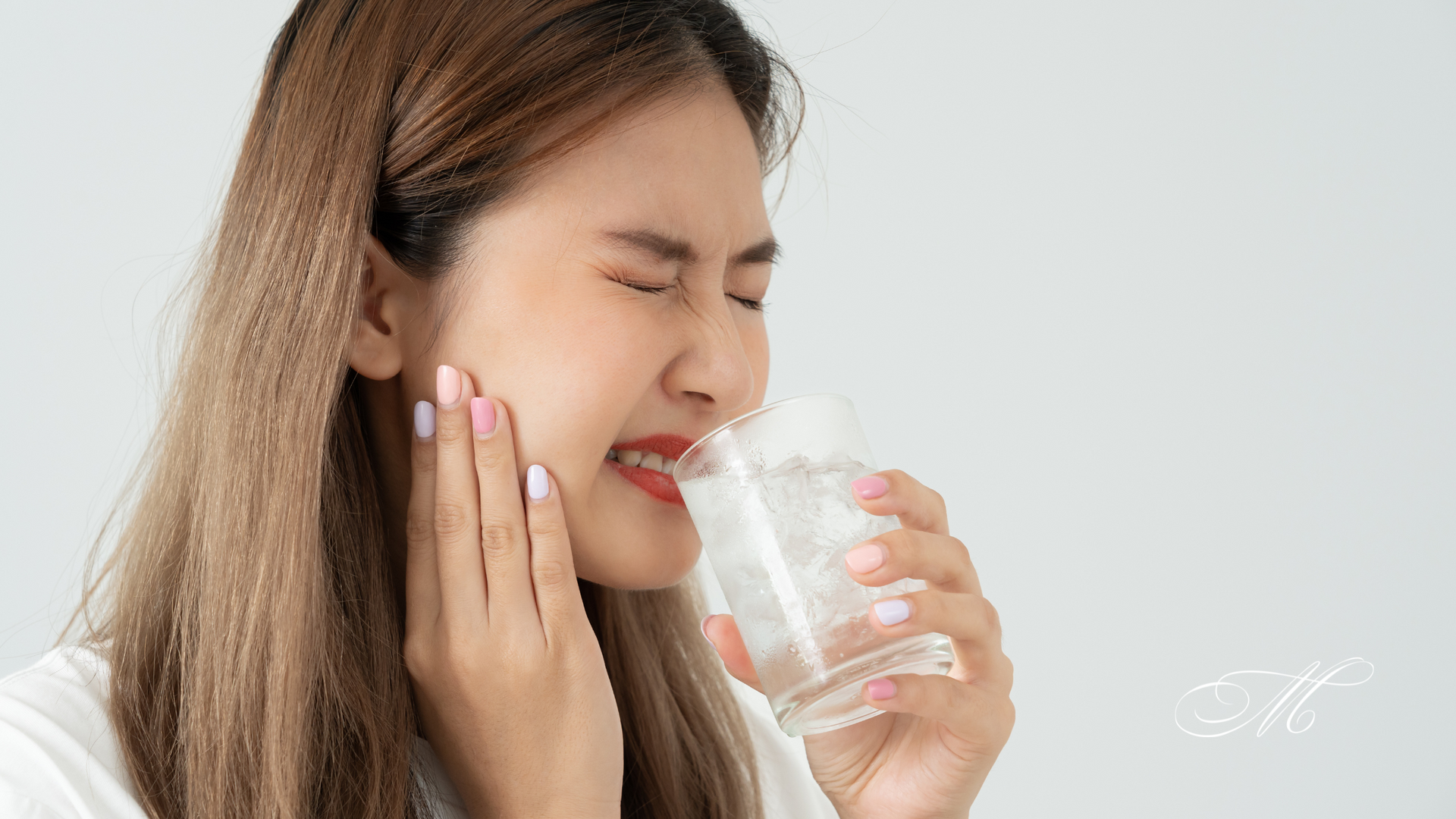 A woman is holding her mouth in pain while drinking a glass of water.