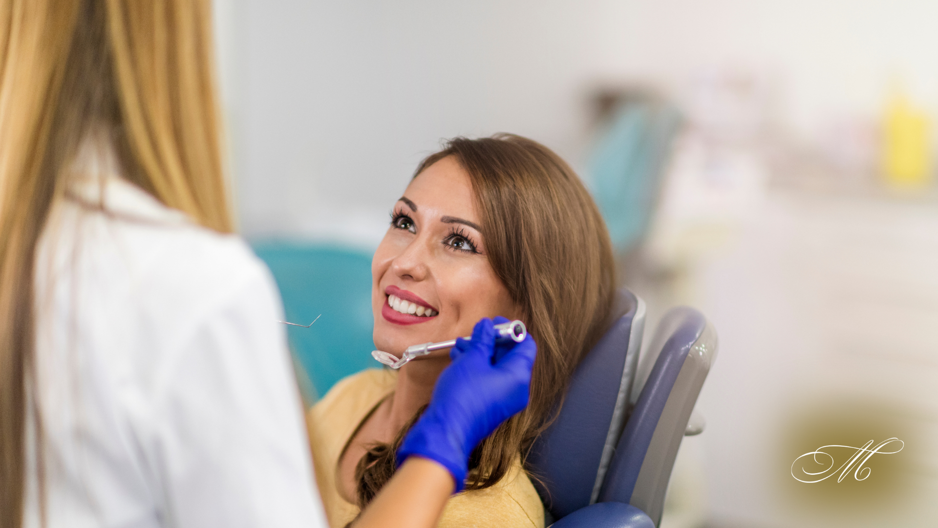 A woman is sitting in a dental chair while a dentist examines her teeth.