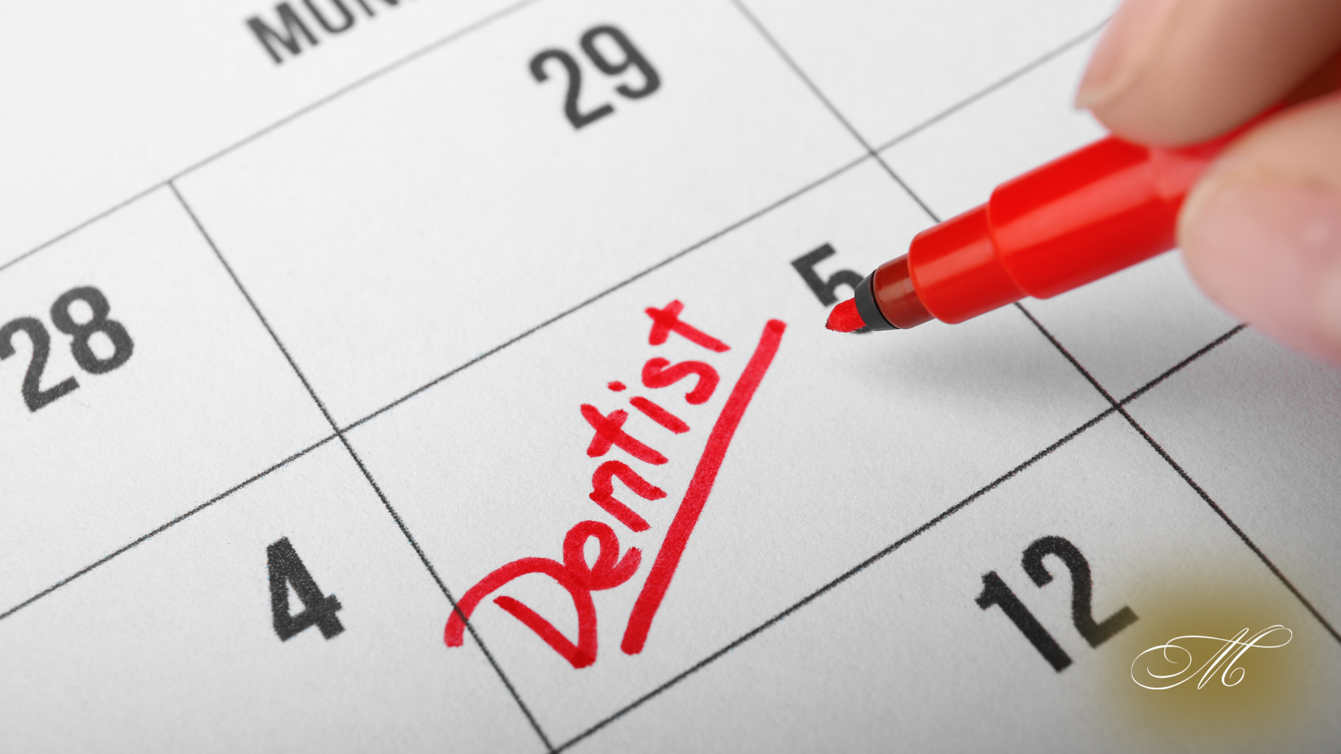 A person is writing the word dentist on a calendar