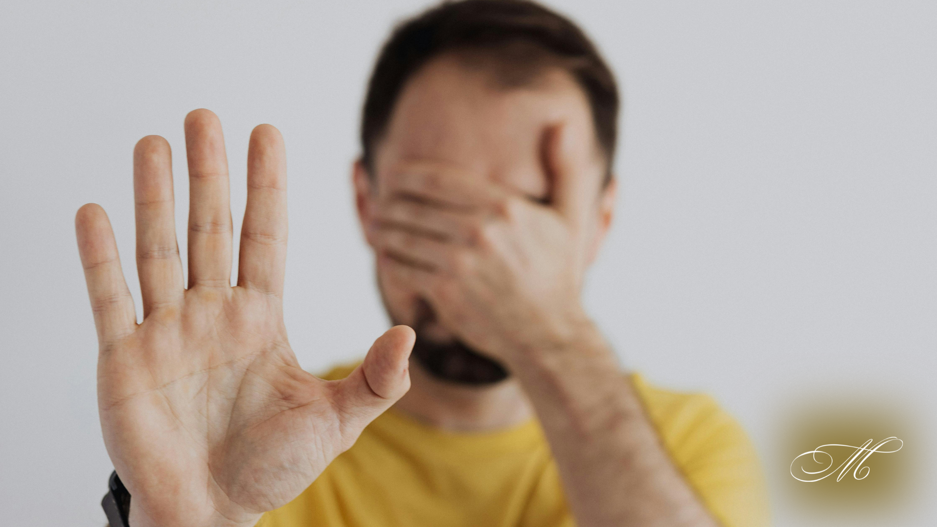 A man is covering his face with his hands and making a stop sign.