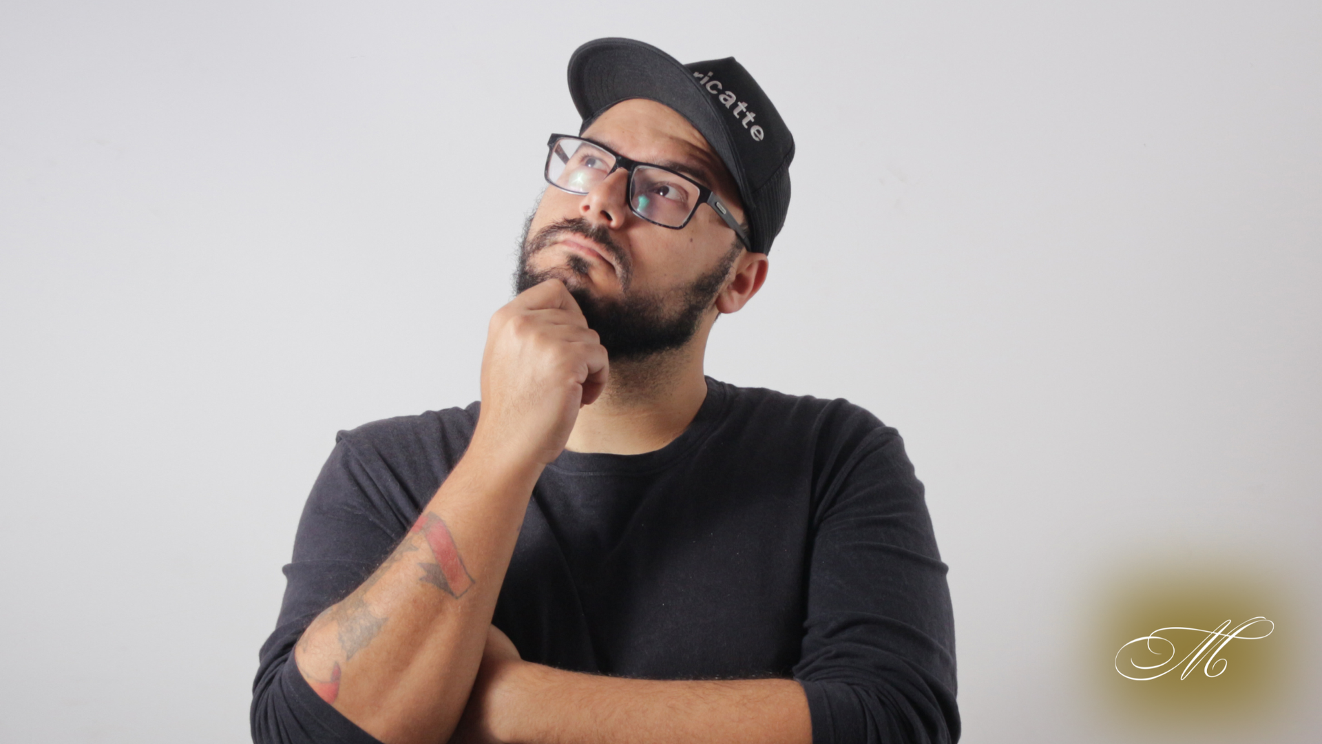 Man in glasses and cap, looking up pensively, hand on chin, against a white background.