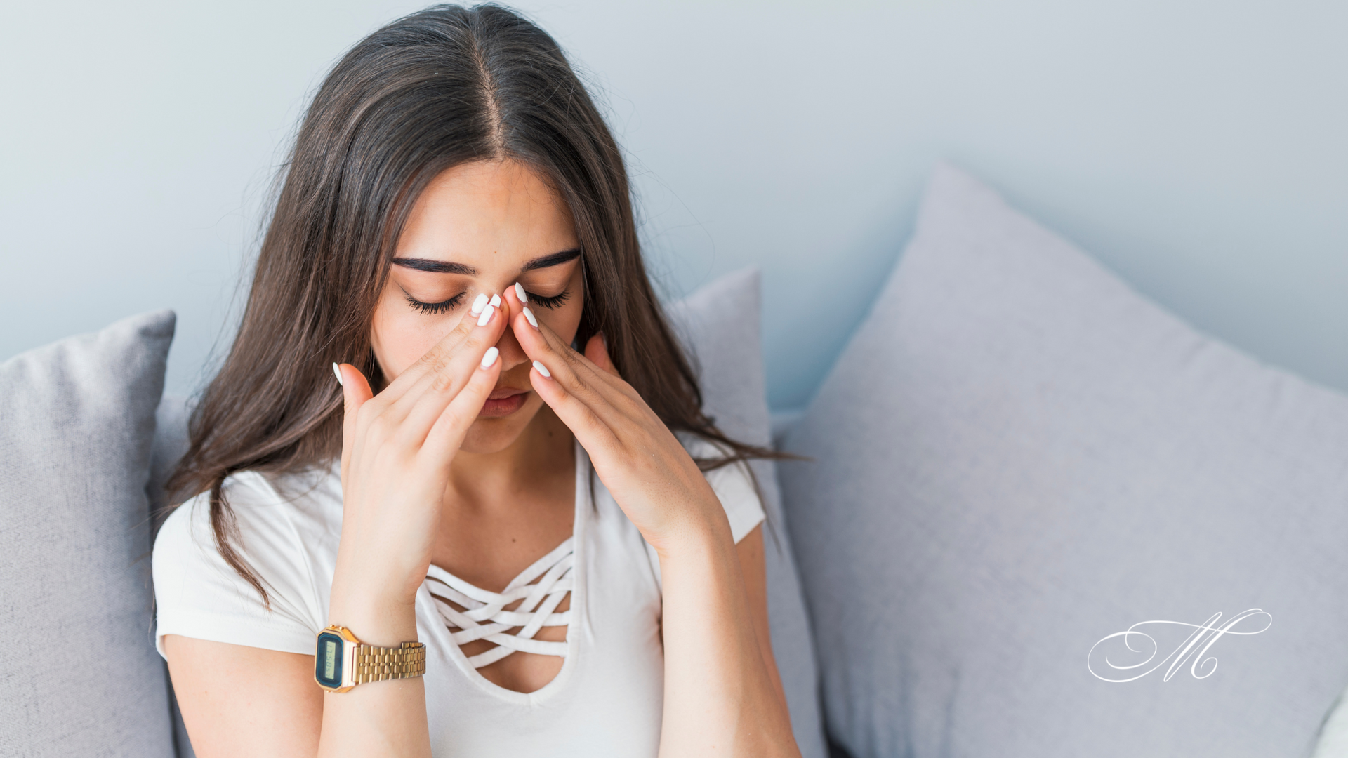 A woman is sitting on a couch covering her face with her hands.