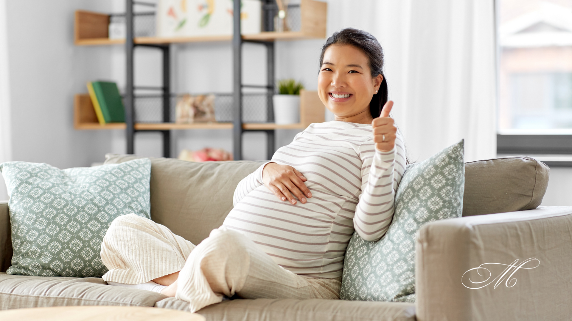 A pregnant woman is sitting on a couch and giving a thumbs up.