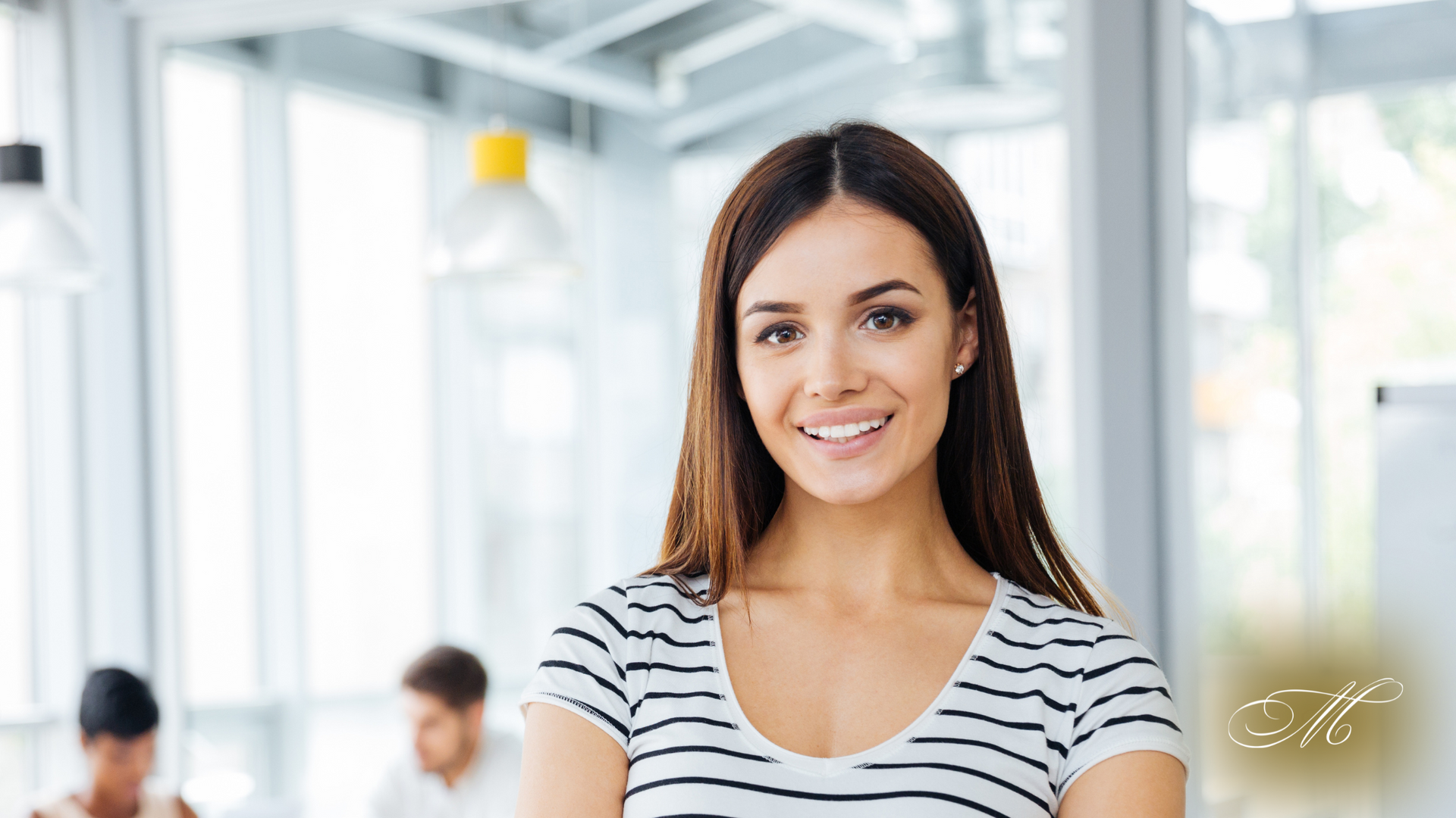 A woman in a striped shirt is smiling in an office.