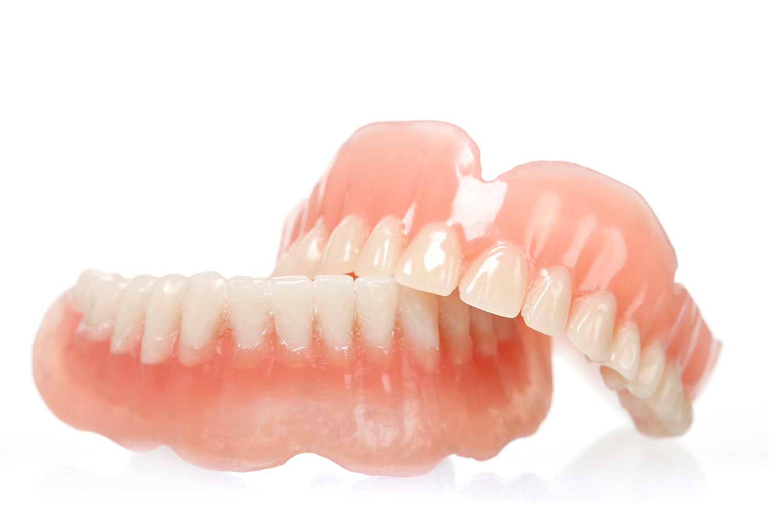 A set of complete upper and lower dentures with white teeth and pink acrylic gums, displayed against a white background.