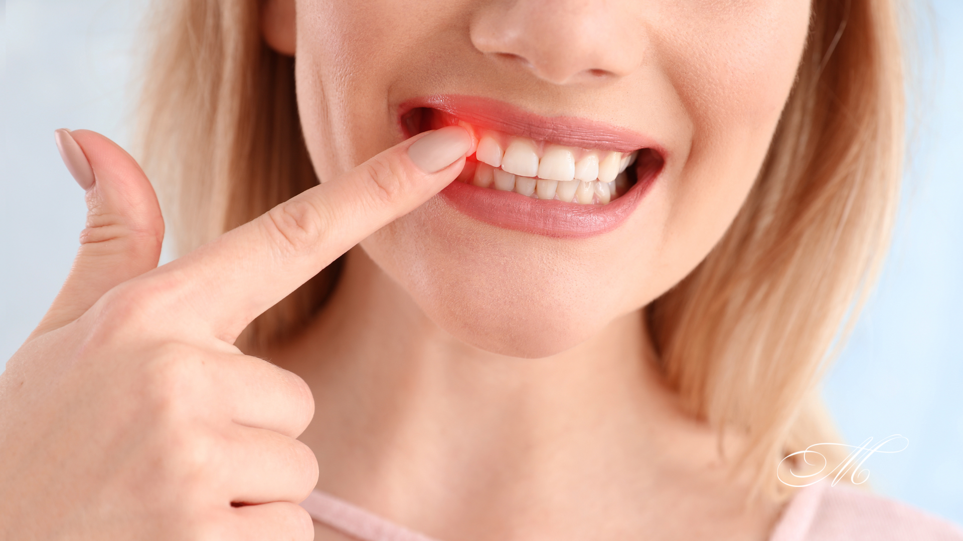 A woman is pointing at her gums with her finger.