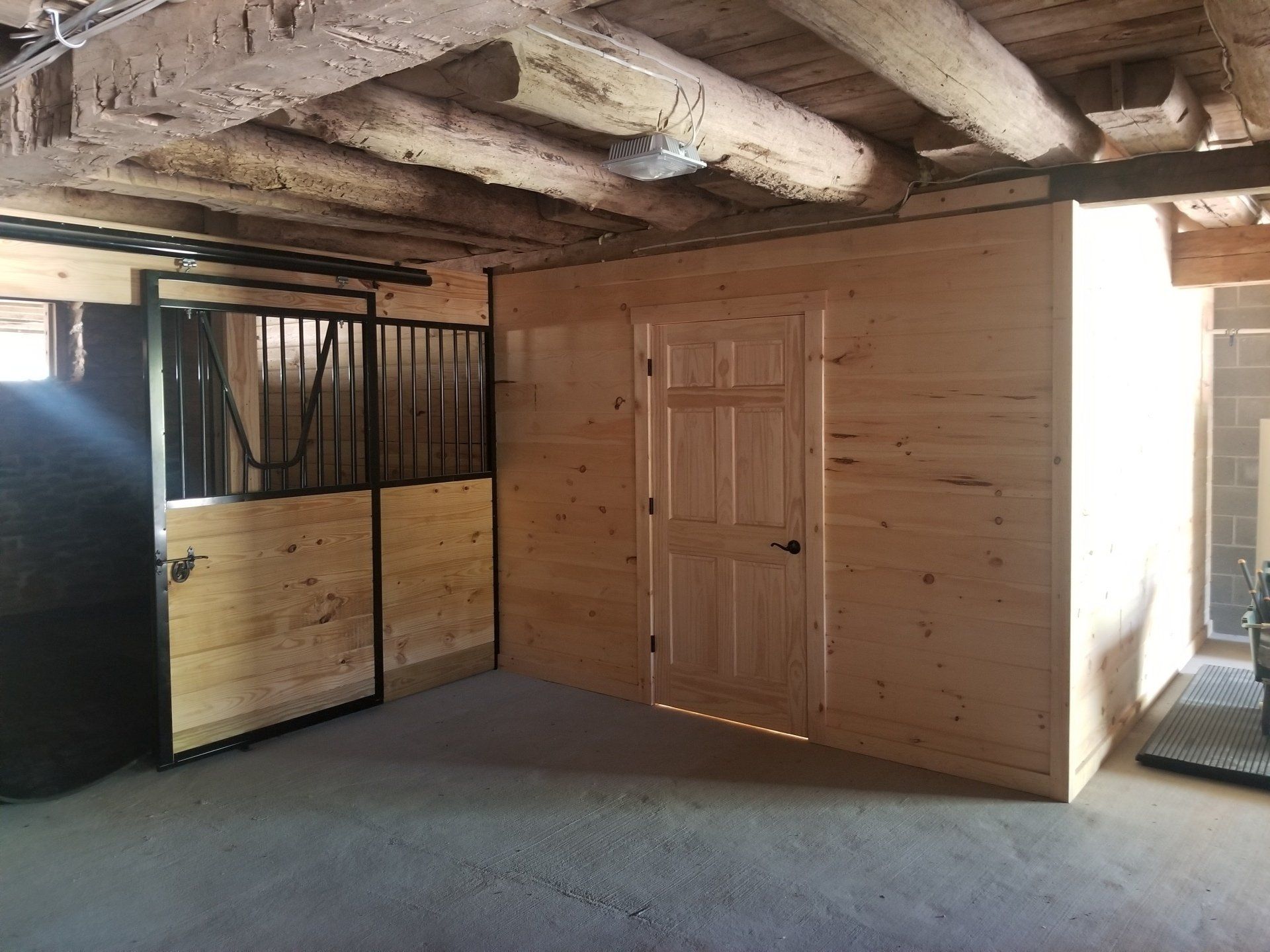 Interior of a barn with a horse stall and a small enclosed room with a door. Wooden beams and walls.
