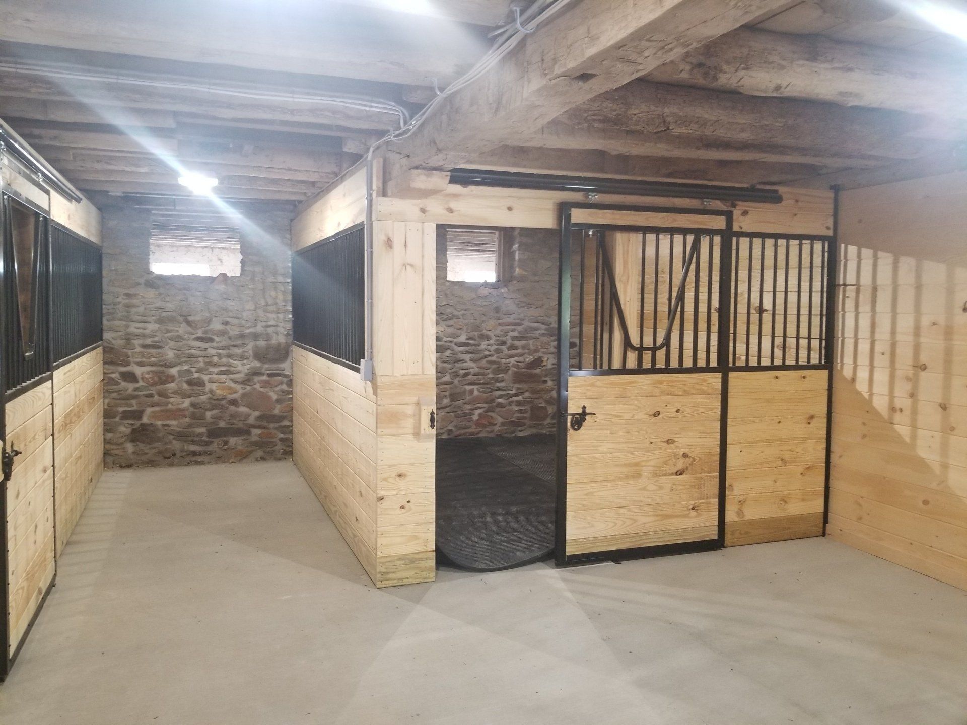 Interior of a barn with wooden stalls and a stone wall. The stalls have metal bars and sliding doors.
