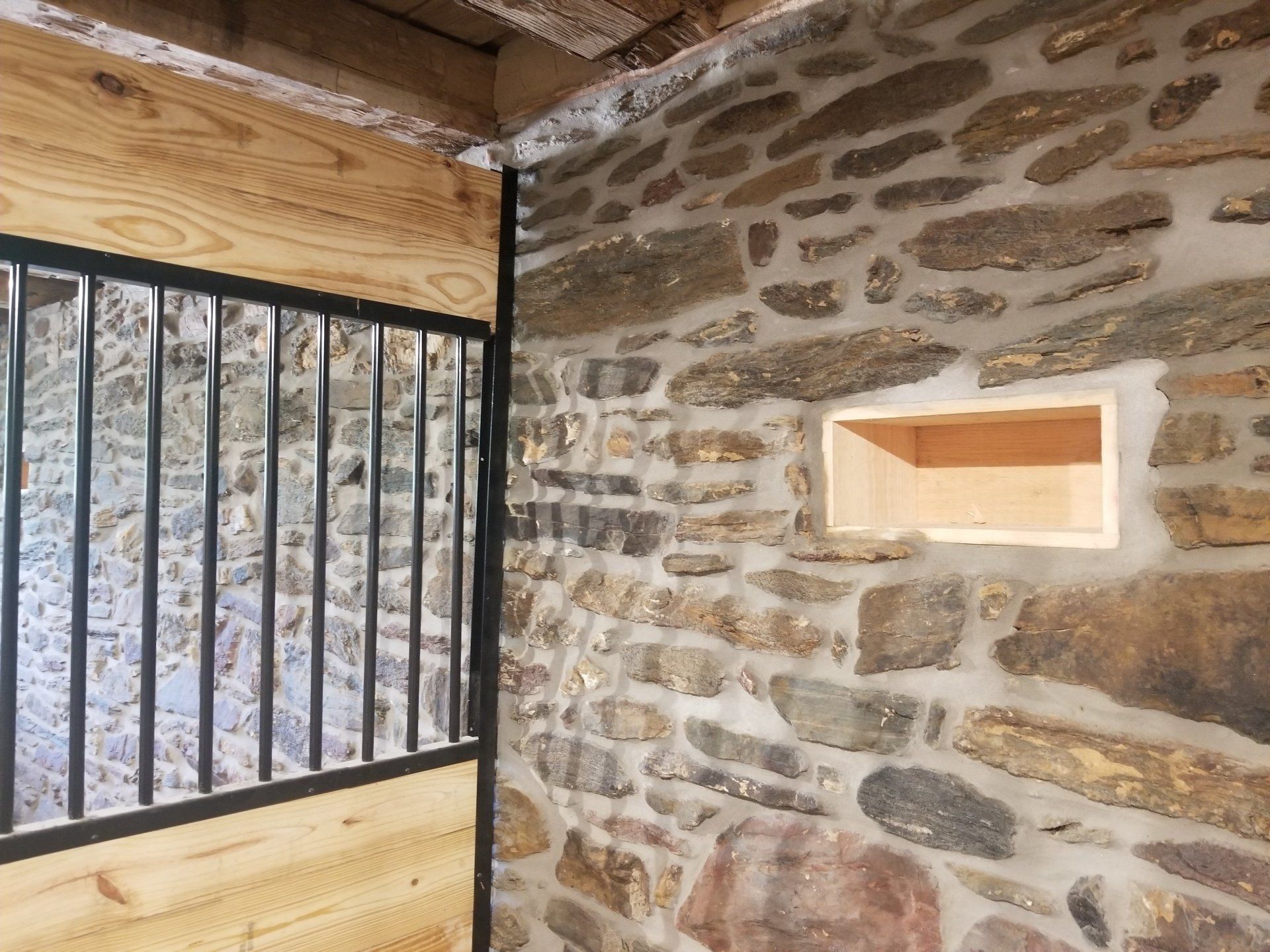 Interior of a barn stall with stone walls, wooden trim, and metal bars.
