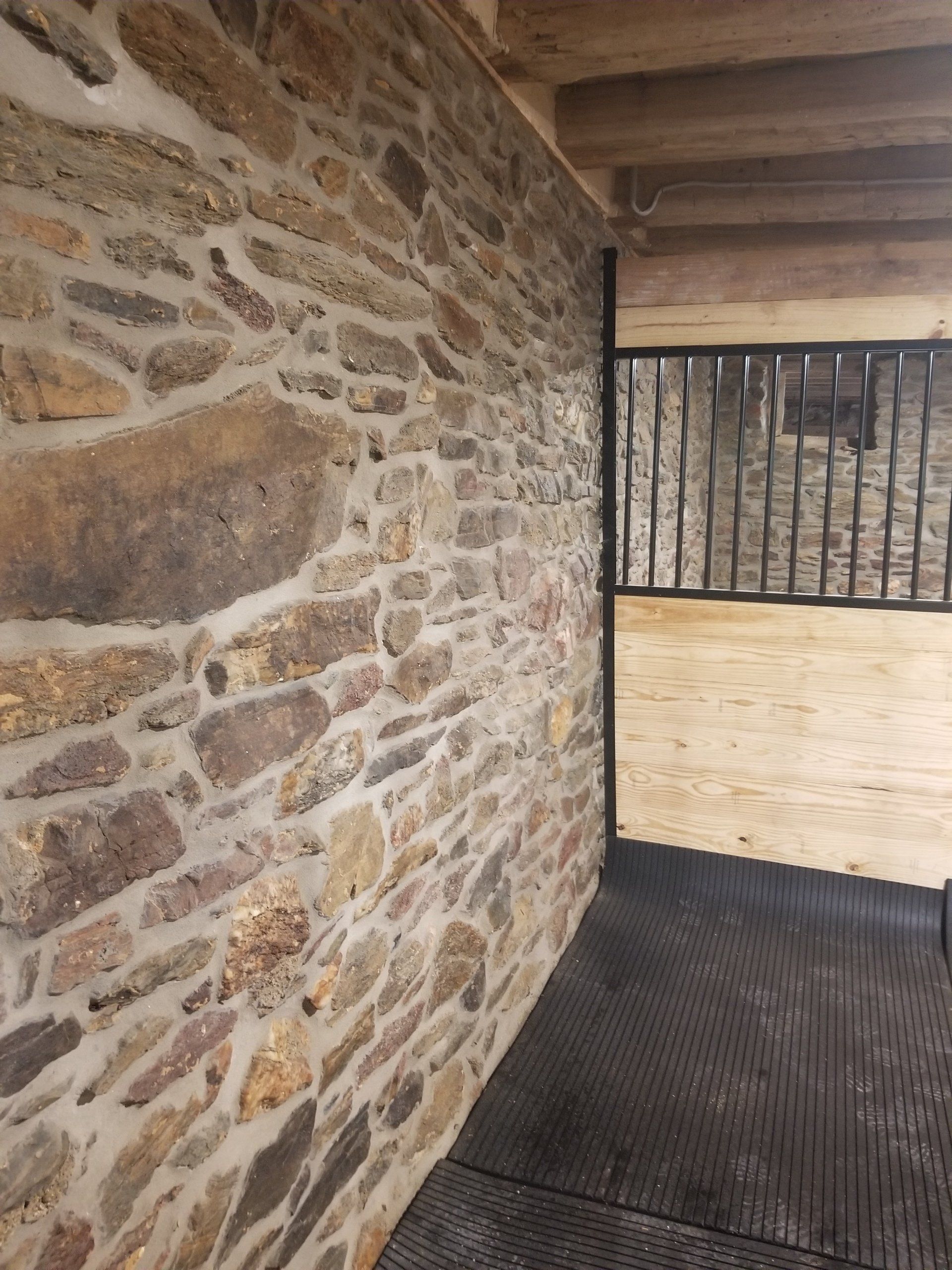 Stone wall inside a barn with a black metal gate and rubber floor.