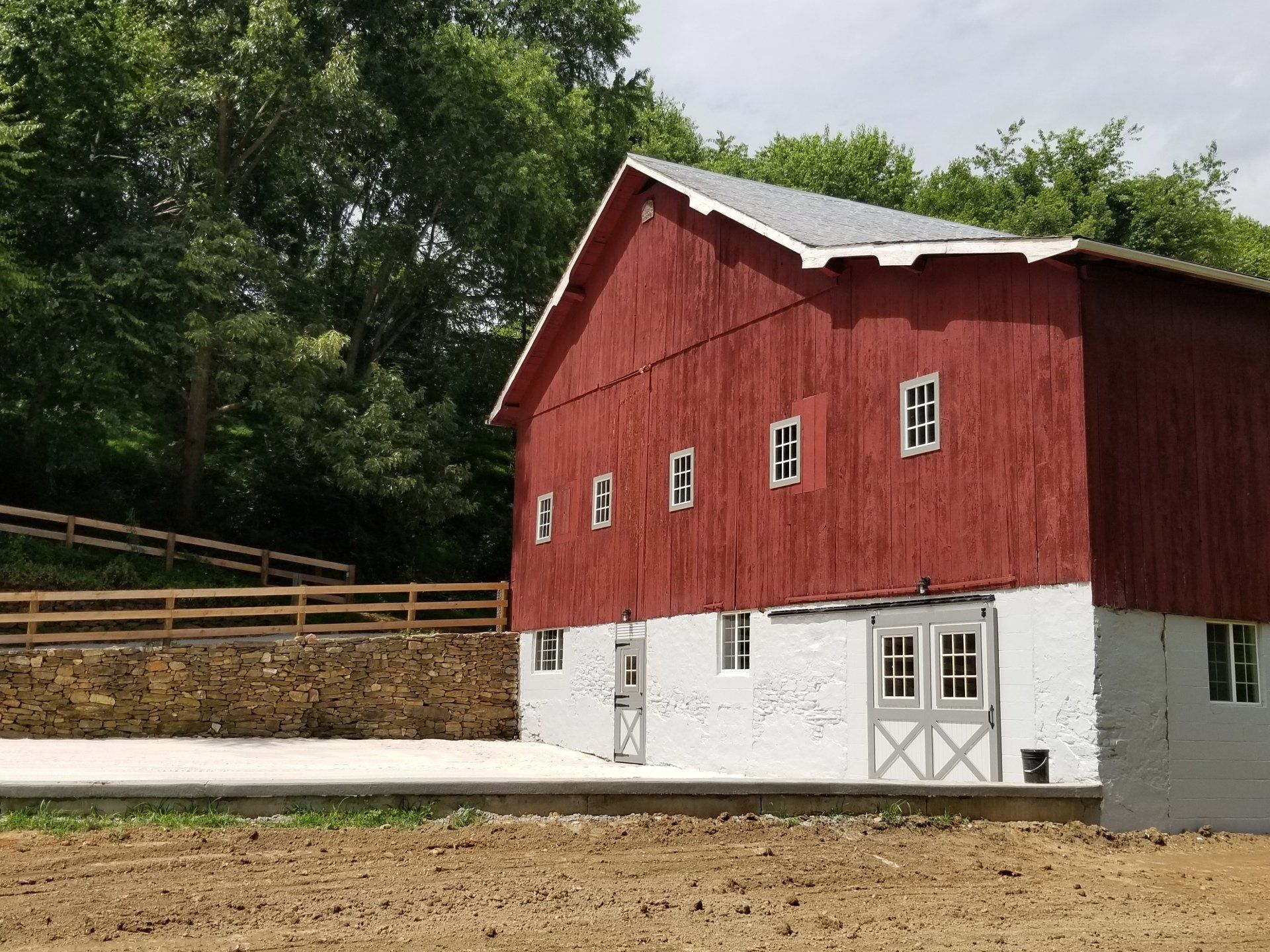 Red barn with white lower section; windows and double doors.  Trees and a fence in background.