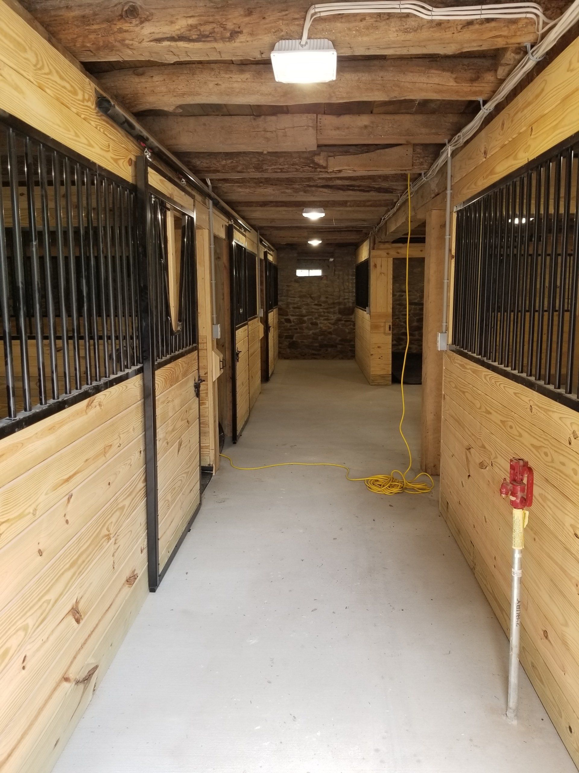 Horse stable hallway with stalls, wooden walls, and a concrete floor.