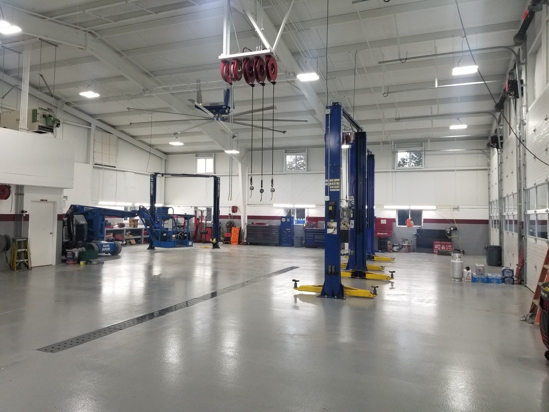 Inside a bright auto repair shop; several blue car lifts and overhead equipment are visible.