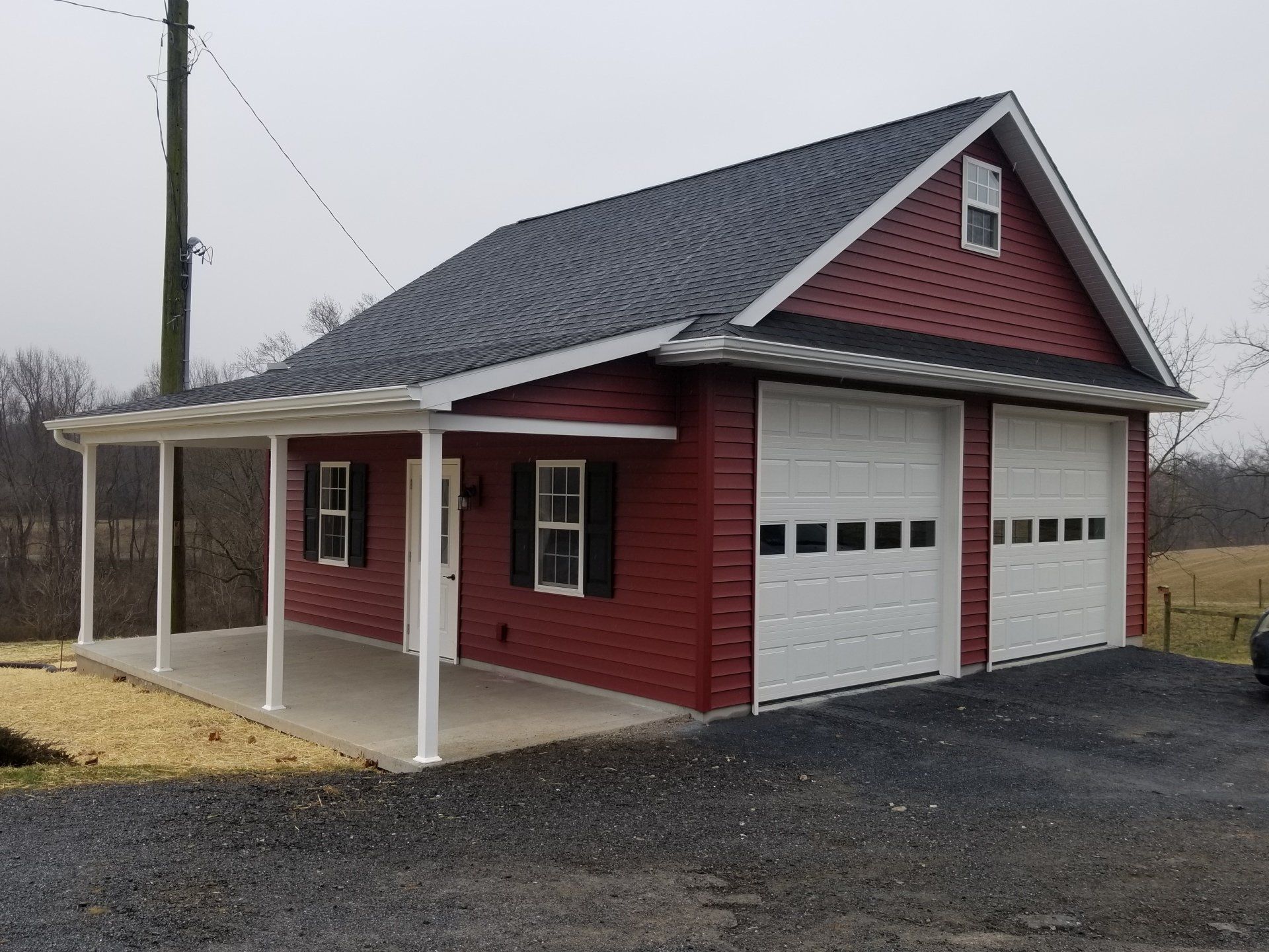 Red two-car garage with a porch. Features white doors, black shutters, and a dark roof. Located outdoors.