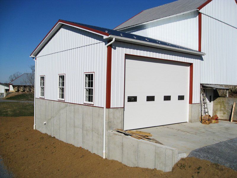 White barn with red trim and a large garage door on a concrete foundation.
