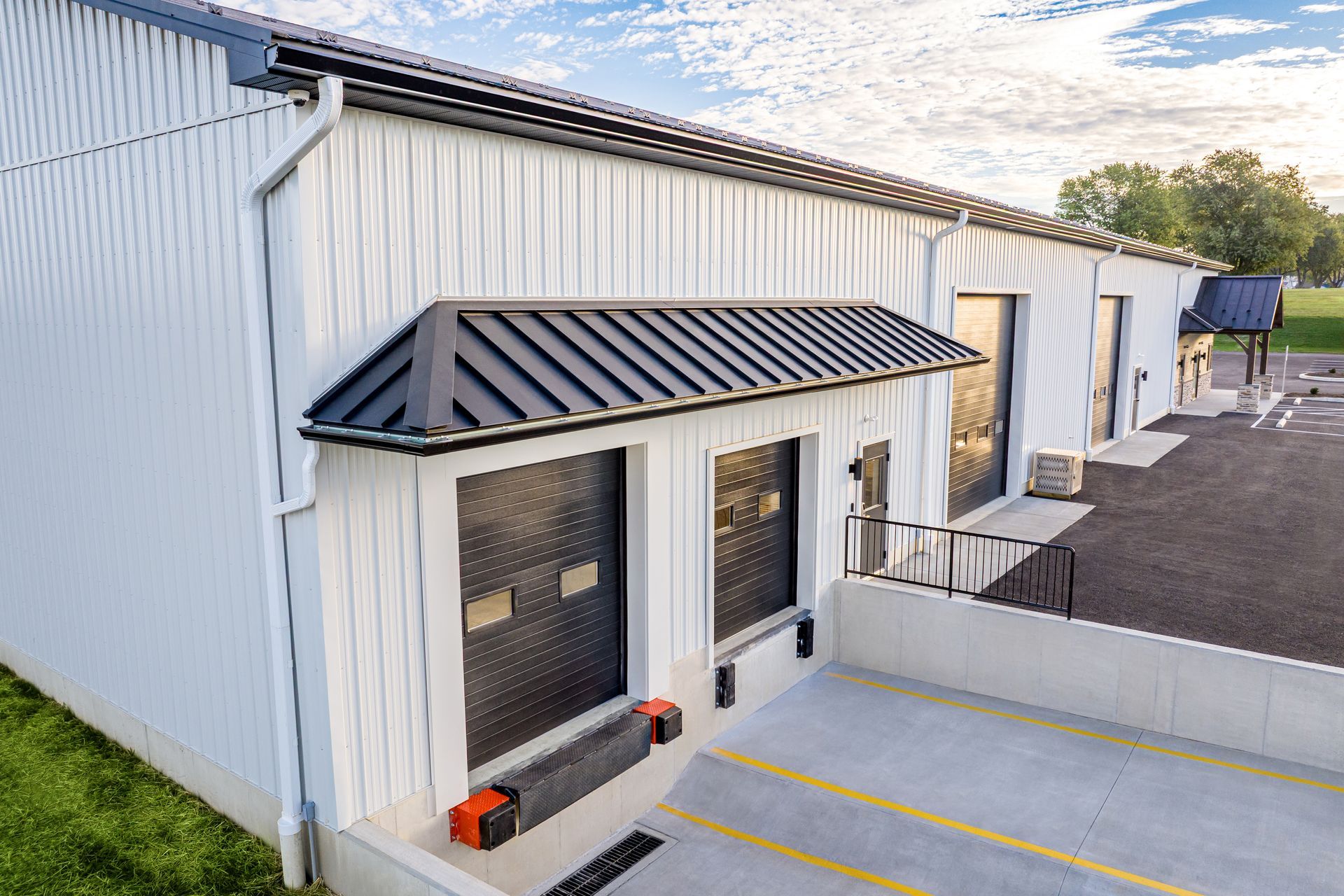 White industrial building with black awning and loading docks under a partly cloudy sky.