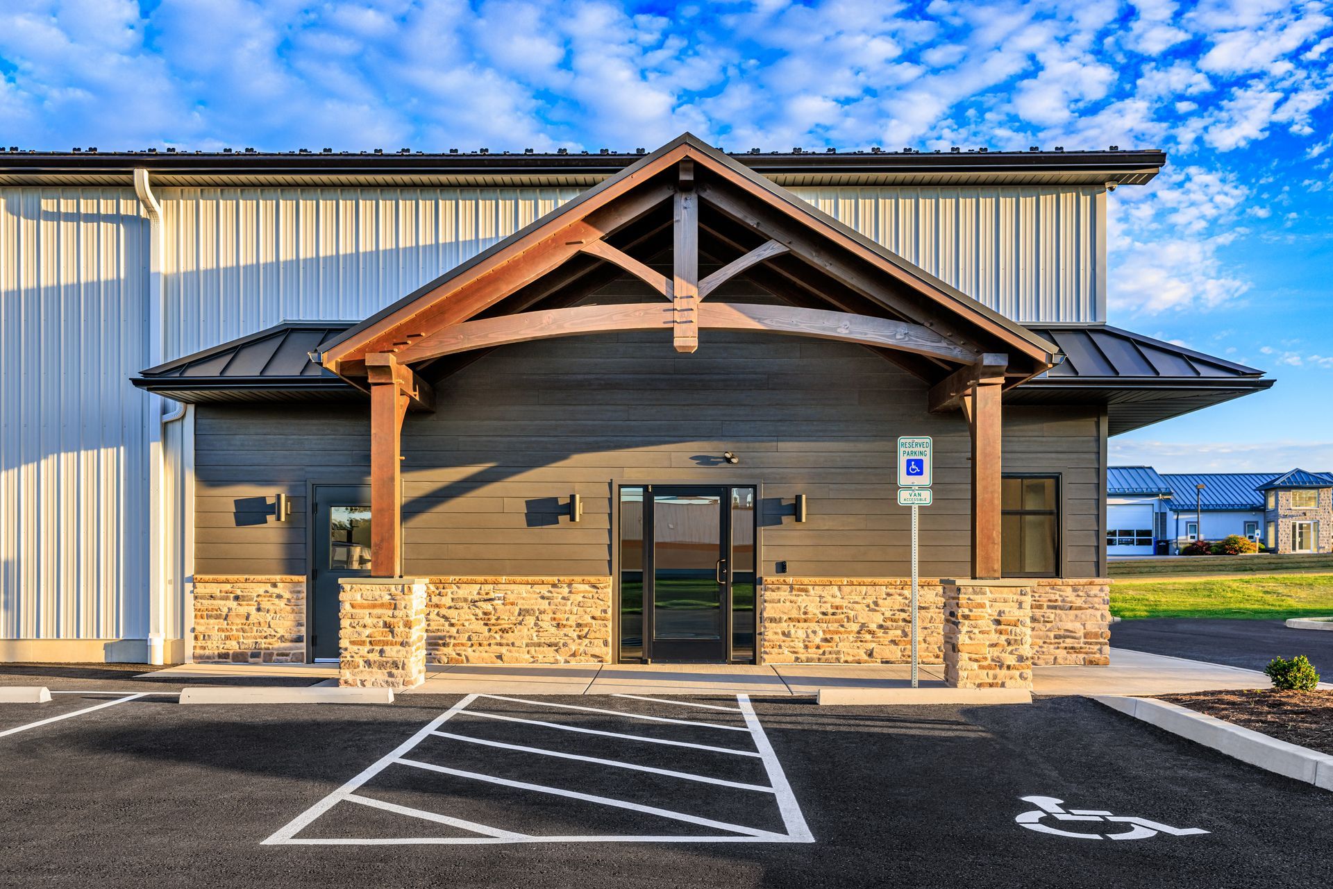Exterior of a modern building with a handicap parking space, brown wood entryway, and tan stone accents.