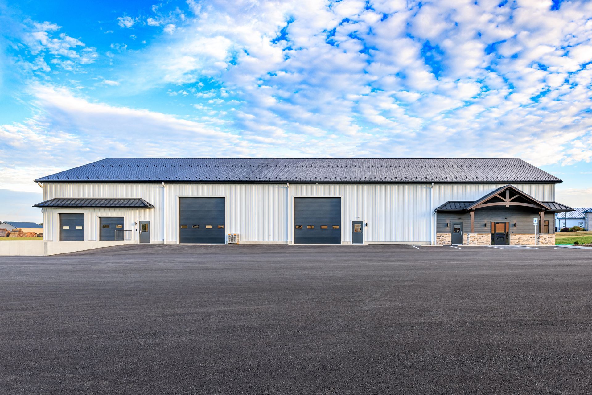 White industrial building with gray garage doors and a small wooden entrance under a blue cloudy sky.