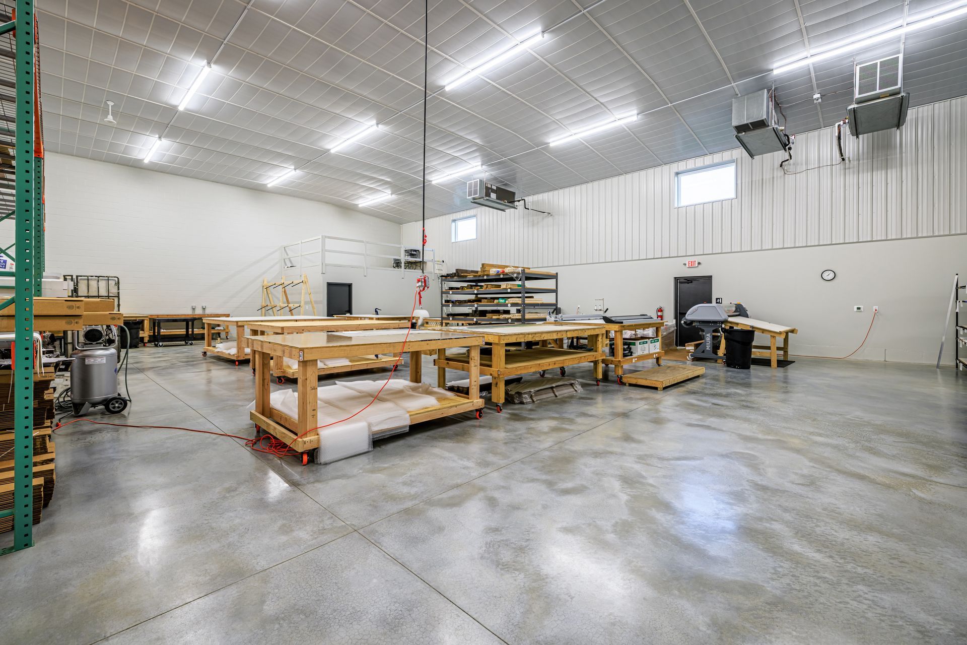 Large, bright workshop with several wooden workbenches, concrete floor, and overhead lighting.