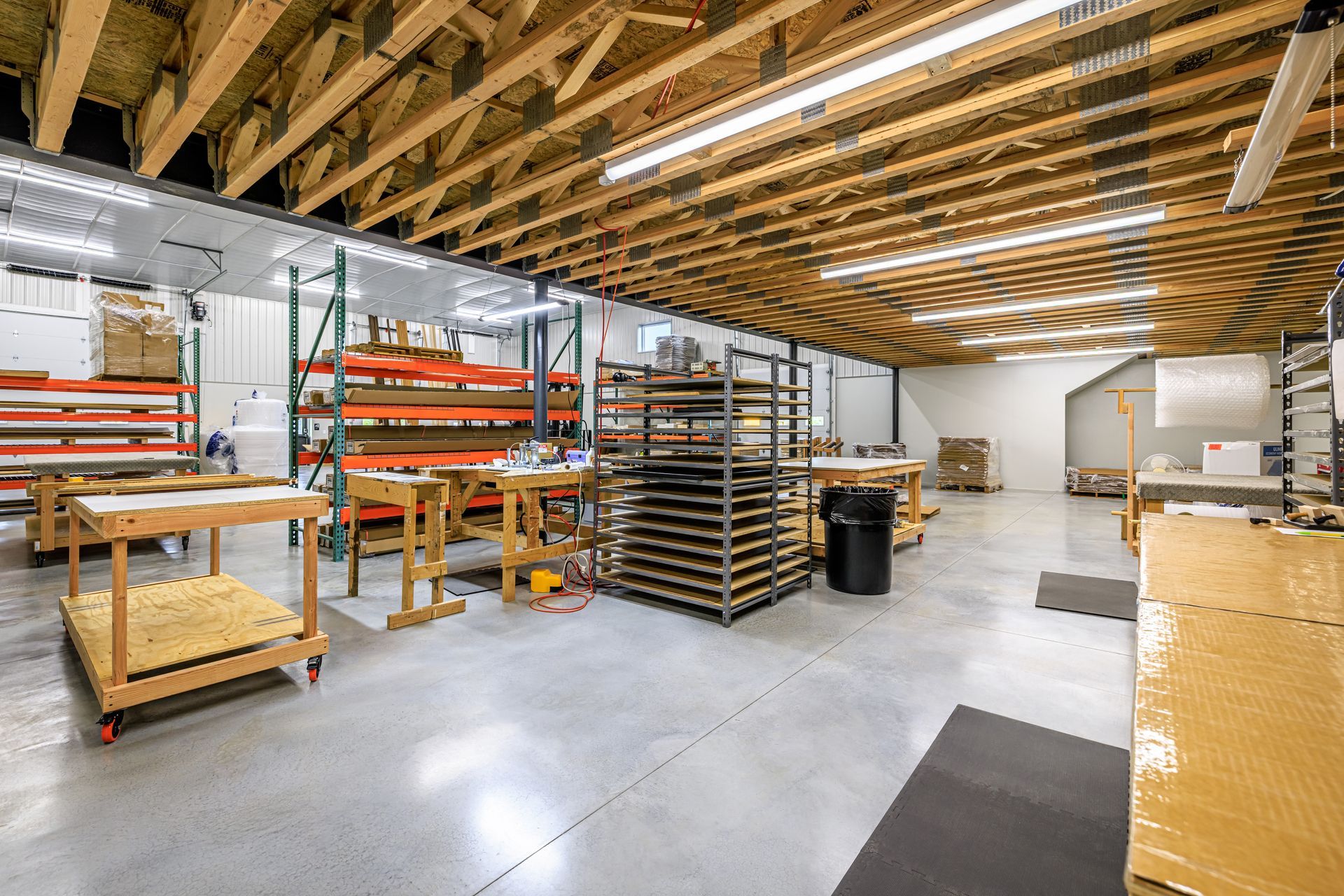 Workshop interior with shelving, worktables, and wooden beams.