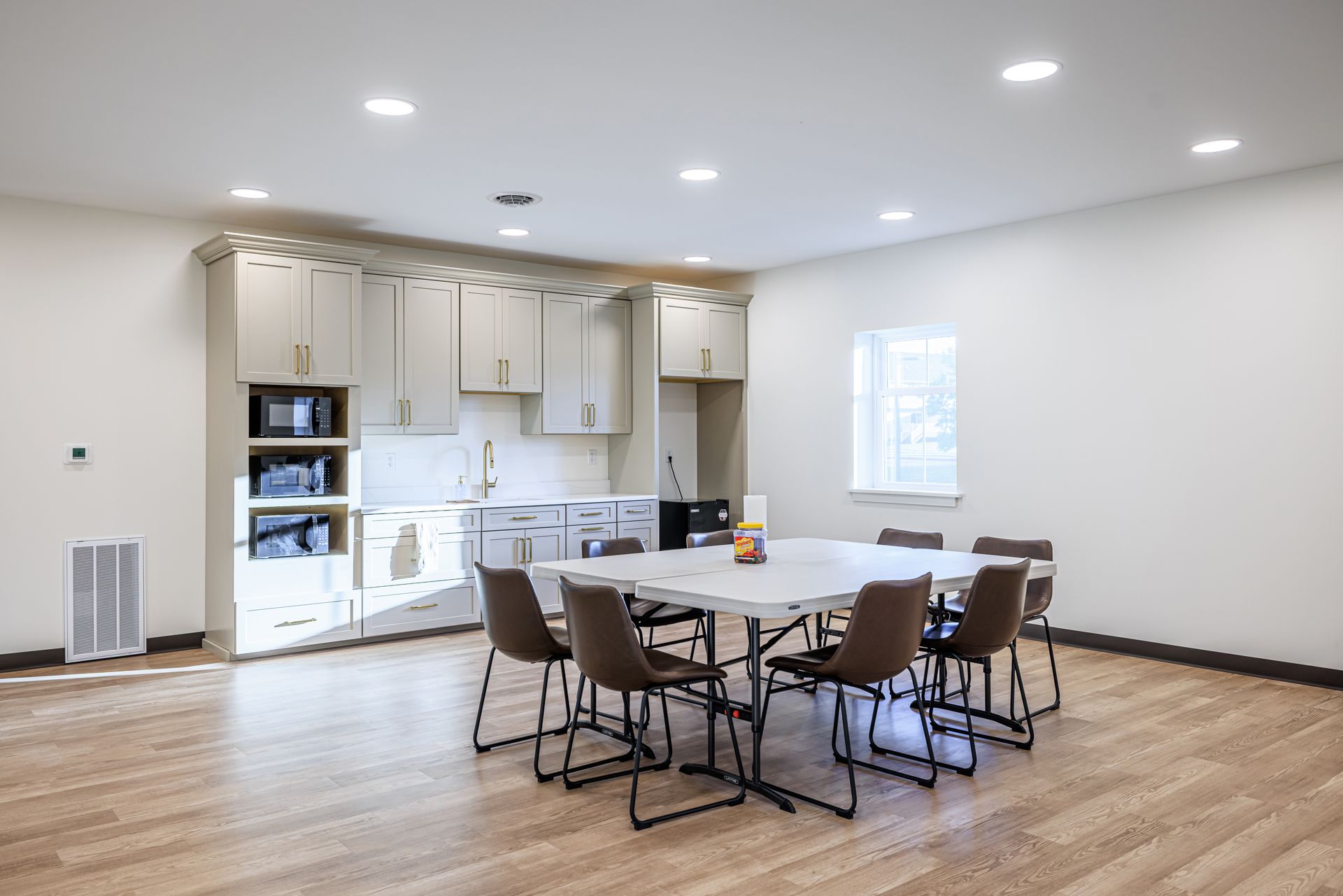 Room with kitchen, table with chairs, and wooden floor. Neutral colors.
