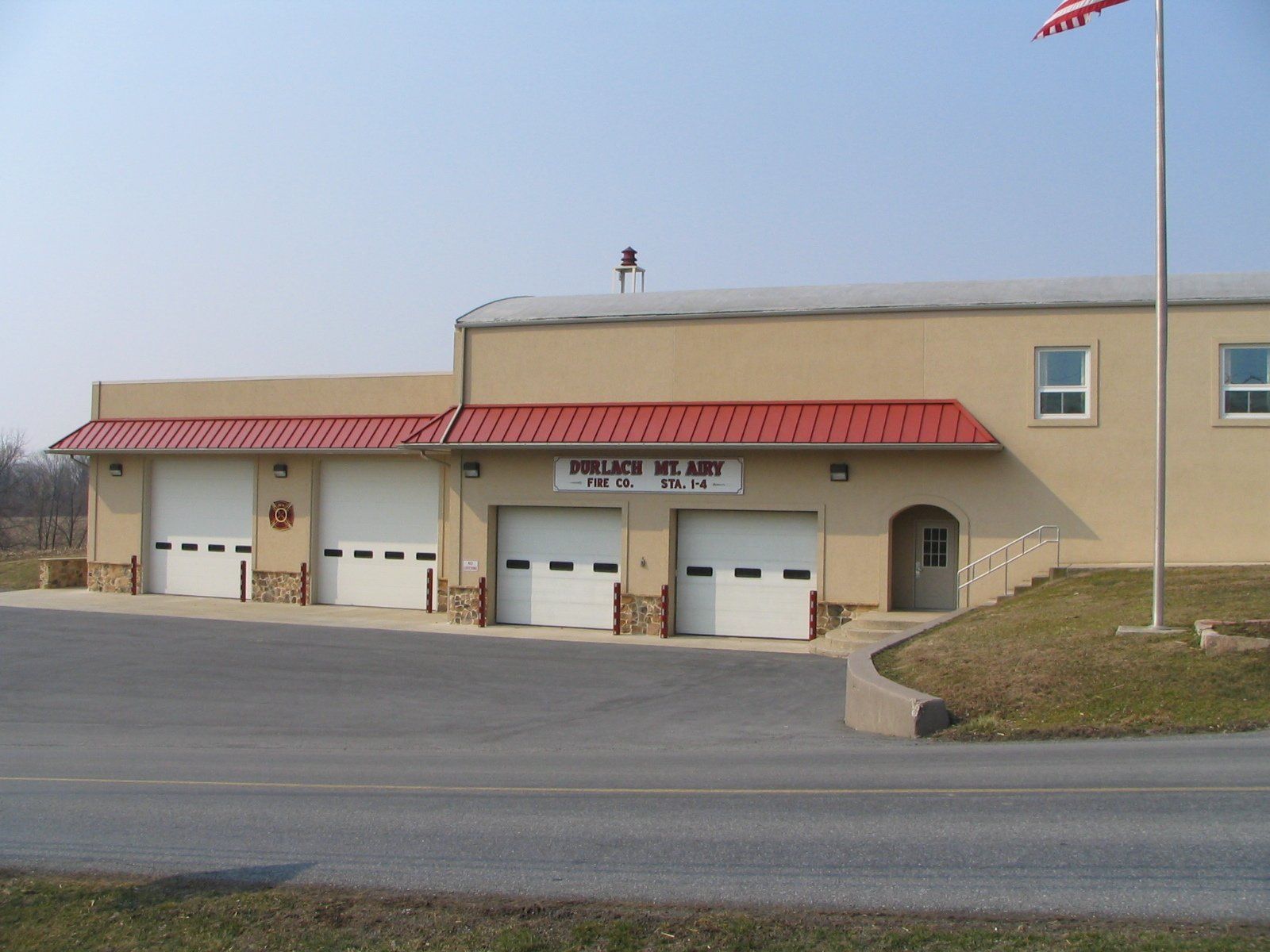 Fire station with three garage doors and red trim. An American flag flies beside it.