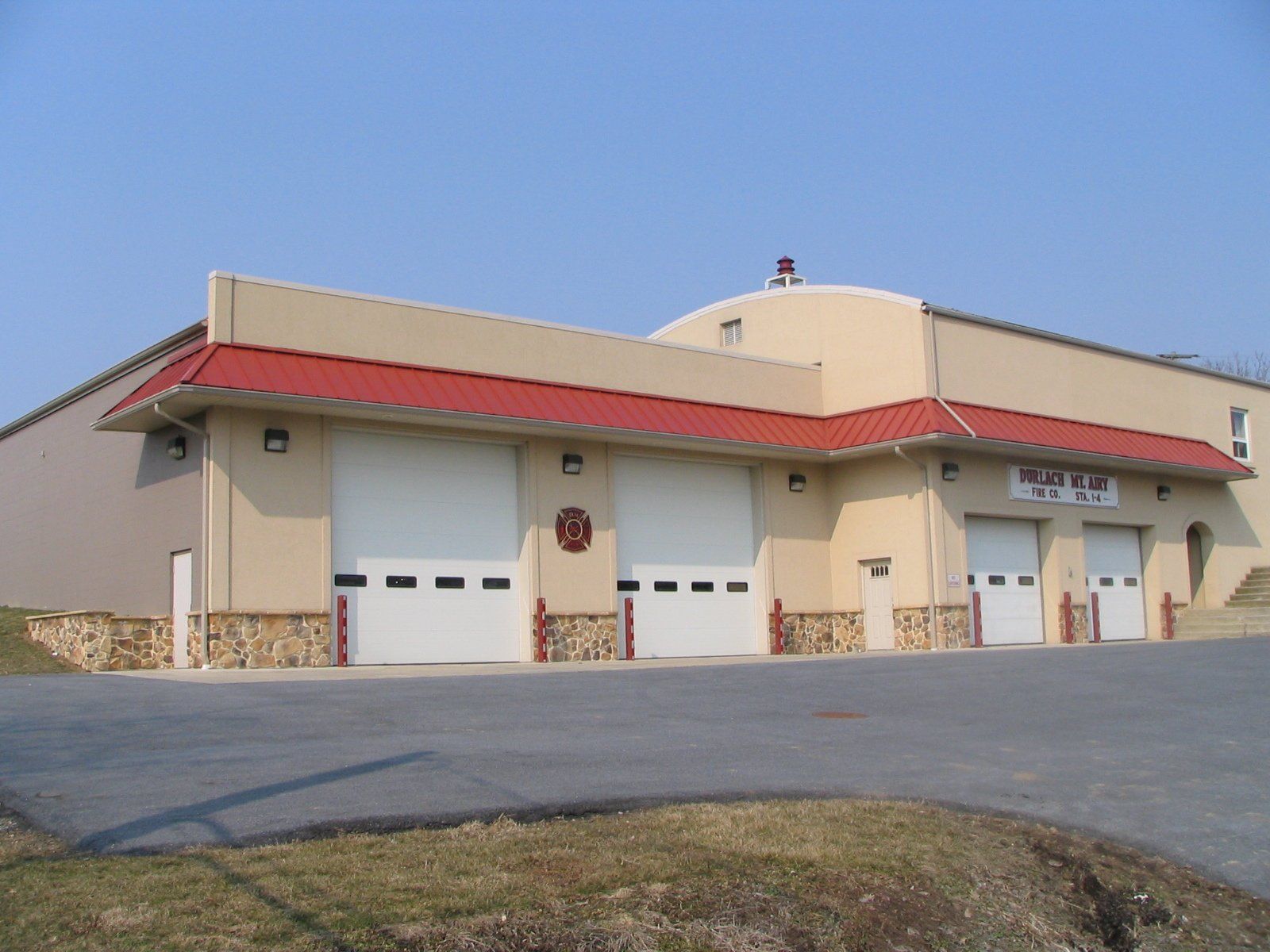 Fire station with three garage doors, tan exterior, red roof.