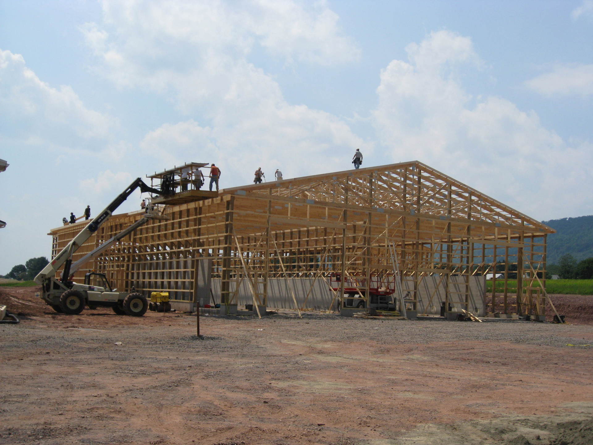 Construction workers on a partially built wooden structure. A lift is being used, under a blue sky.