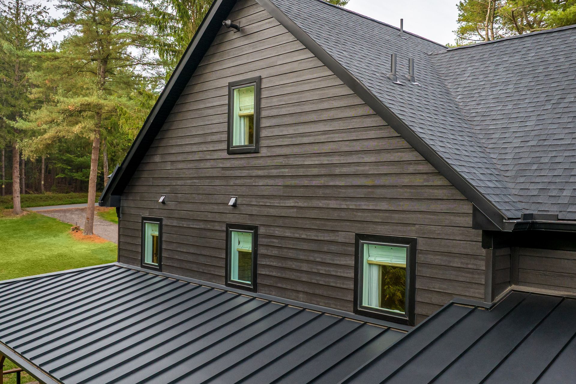 Dark gray house with black trim and roof, set among trees and green grass.