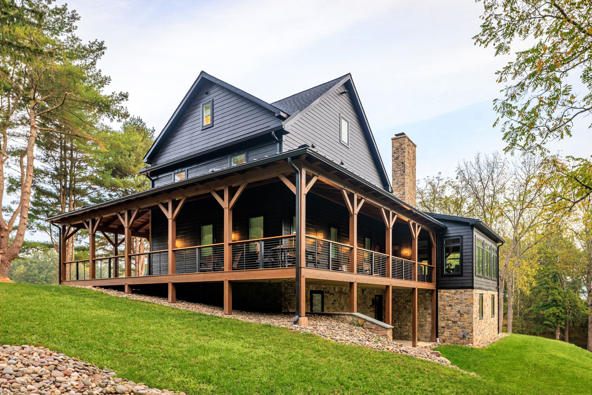 Two-story house with a large porch and black exterior, set on a grassy hill.
