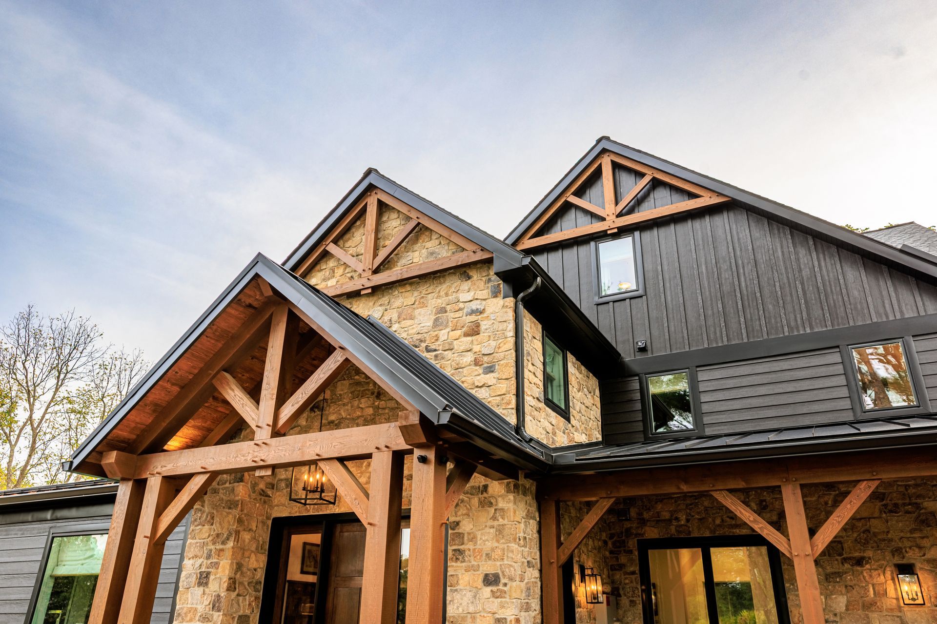 Stone and wood cabin with dark roofing and trim against a blue sky.