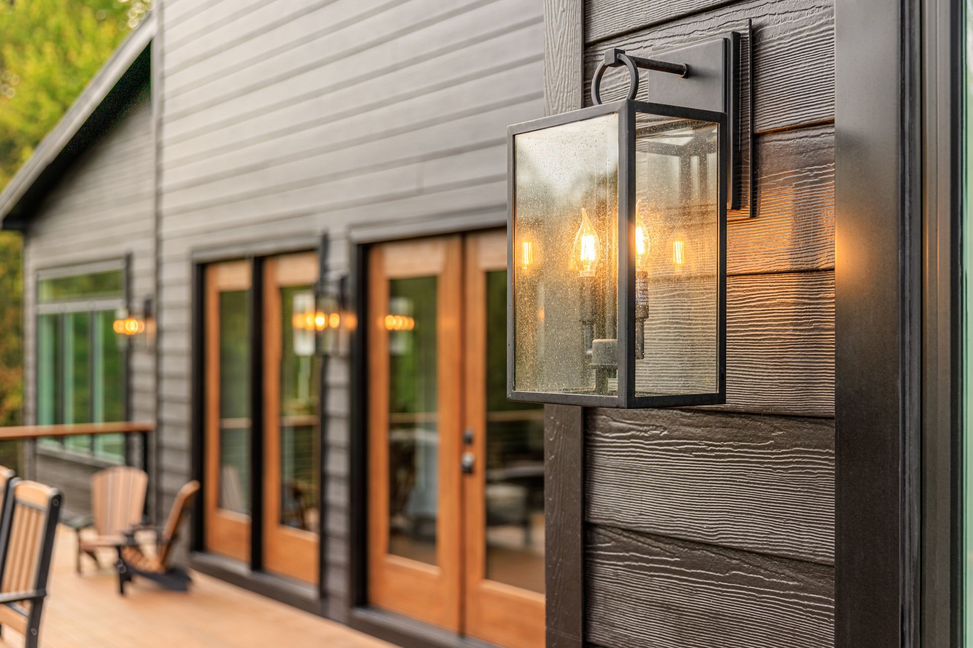 Black house exterior with a wall-mounted lantern illuminating the wooden siding and doors.