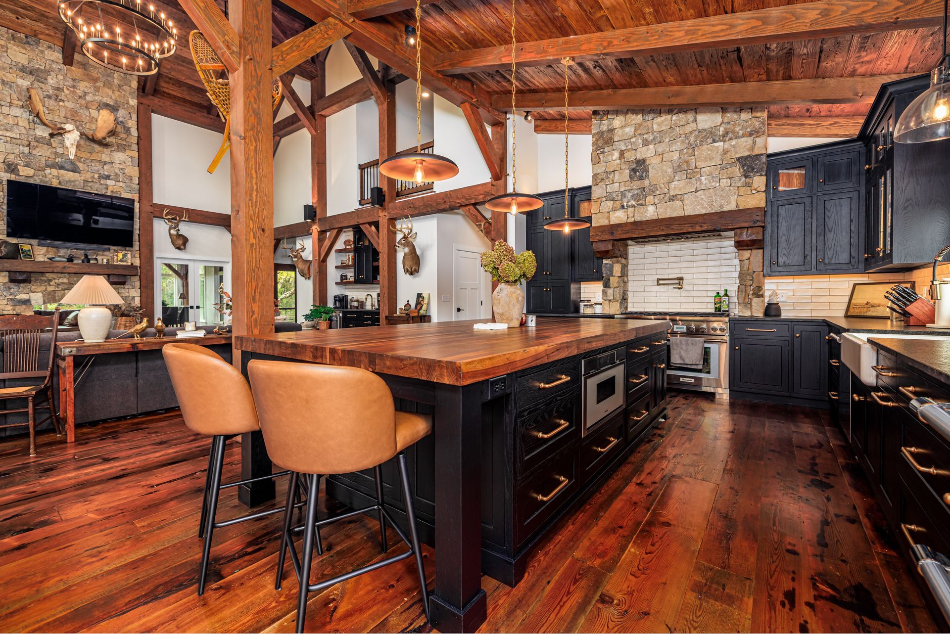 Rustic kitchen with wood beams, stone walls, black cabinets, and large island with bar stools.
