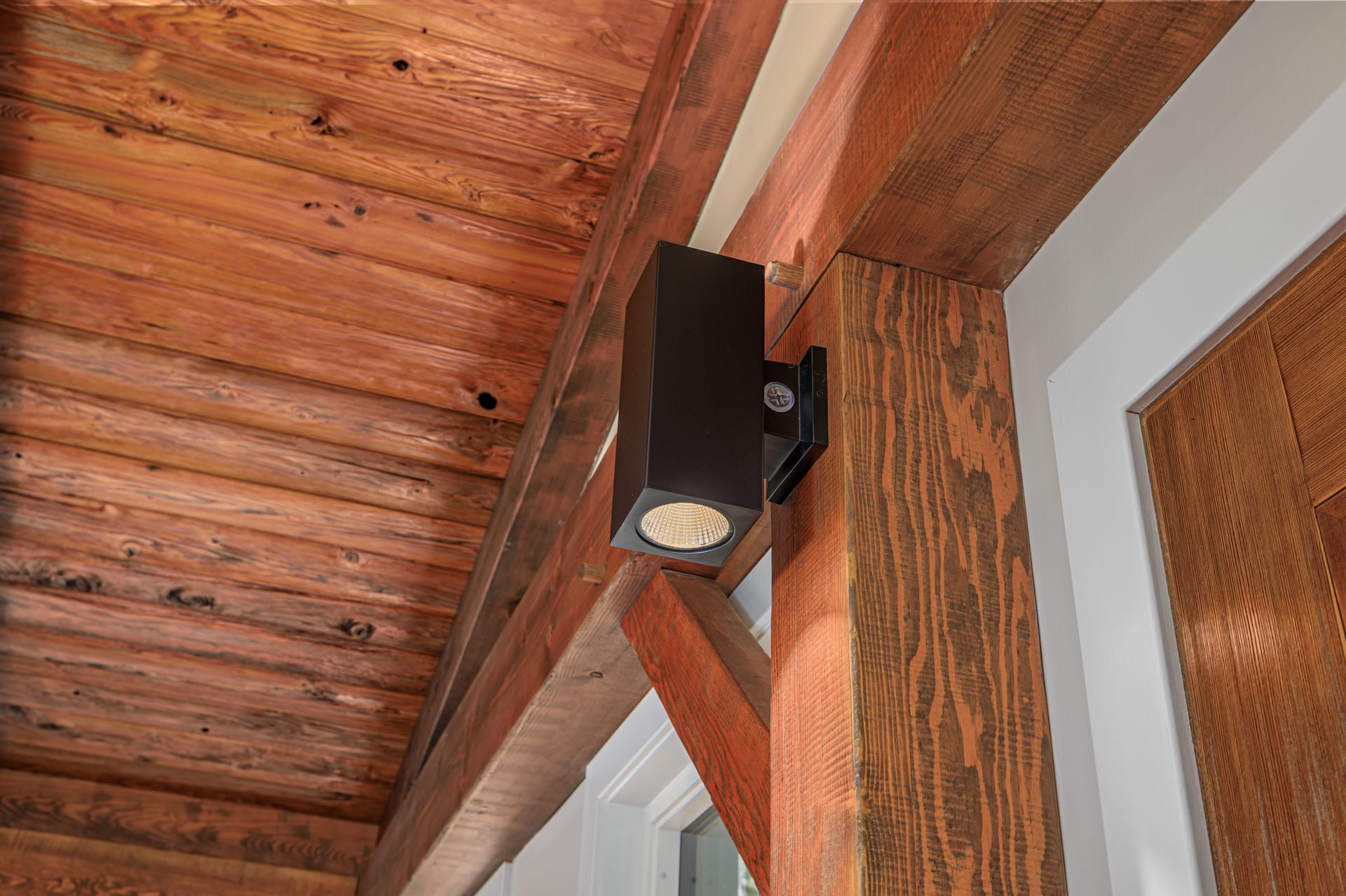 Black outdoor light fixture mounted on wooden porch beam.
