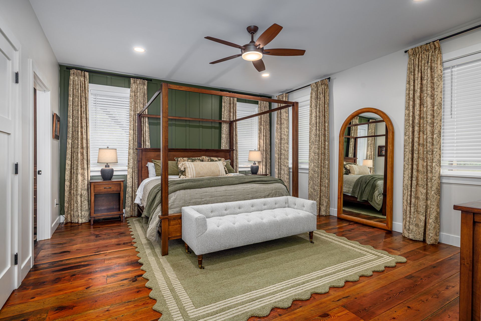 Bedroom with a canopy bed, bench, rug, large mirror, wooden floors, and ceiling fan.