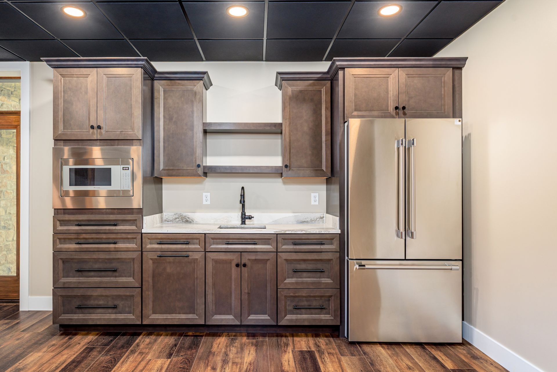 Kitchenette with dark wood cabinets, stainless steel refrigerator and appliances, and a black ceiling.