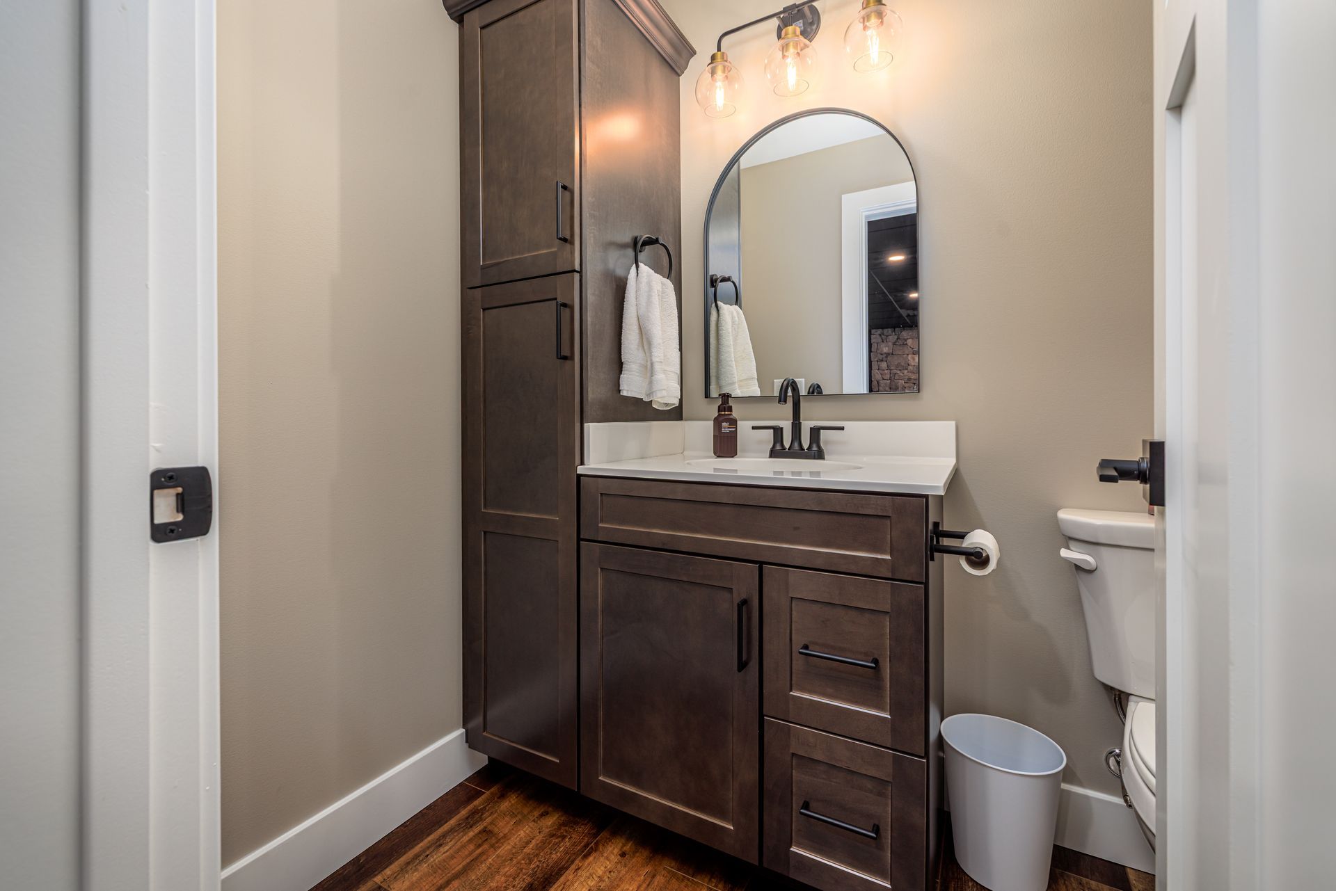 Bathroom with dark cabinetry, white countertop, arched mirror, and toilet.
