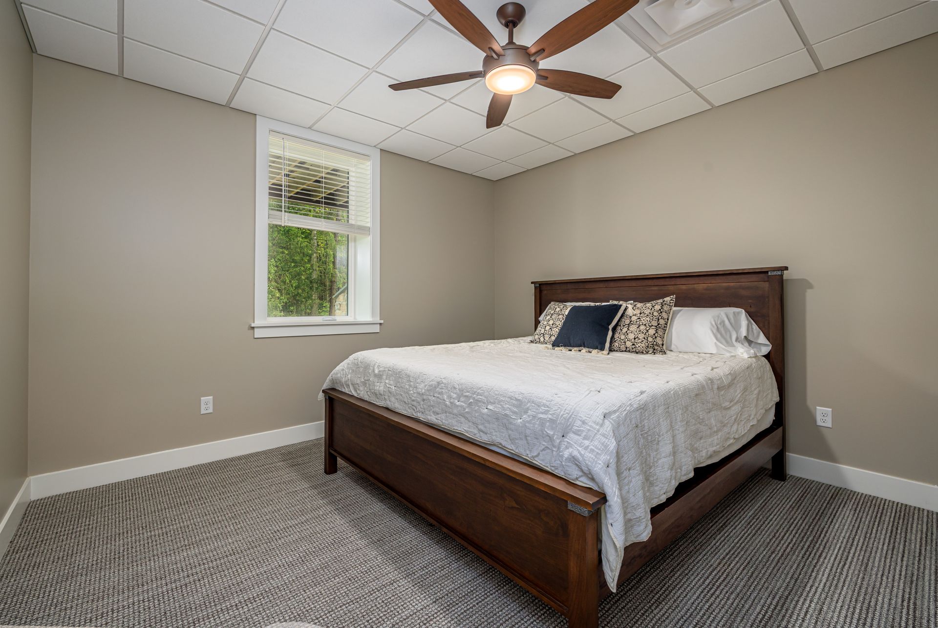 Bedroom with bed, window, ceiling fan, and gray carpet. Neutral walls.