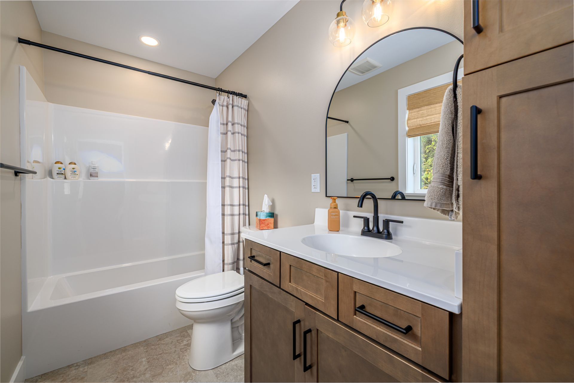Bathroom with a white tub, toilet, and vanity with a brown cabinet and black hardware.