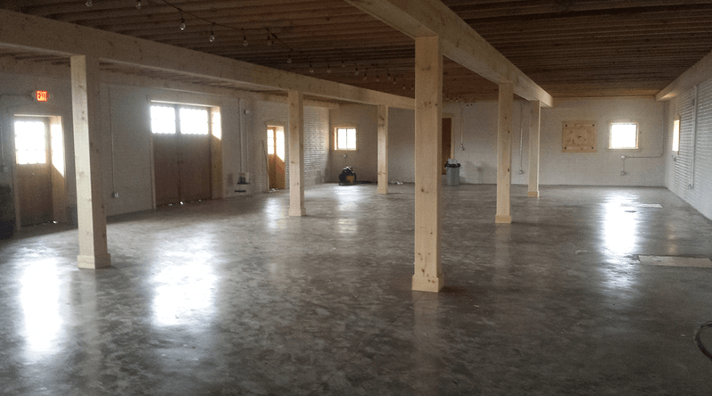 Interior of a large, empty room with polished concrete floor, wooden support beams, and windows.