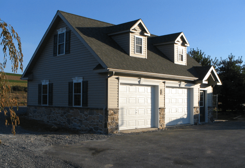 Two-story detached garage with two bays, tan siding, stone base, and two dormers.